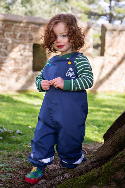 Toddler outside wearing Frugi Waterproof Dungarees in navy blue, made from recycled polyester with fleece lining