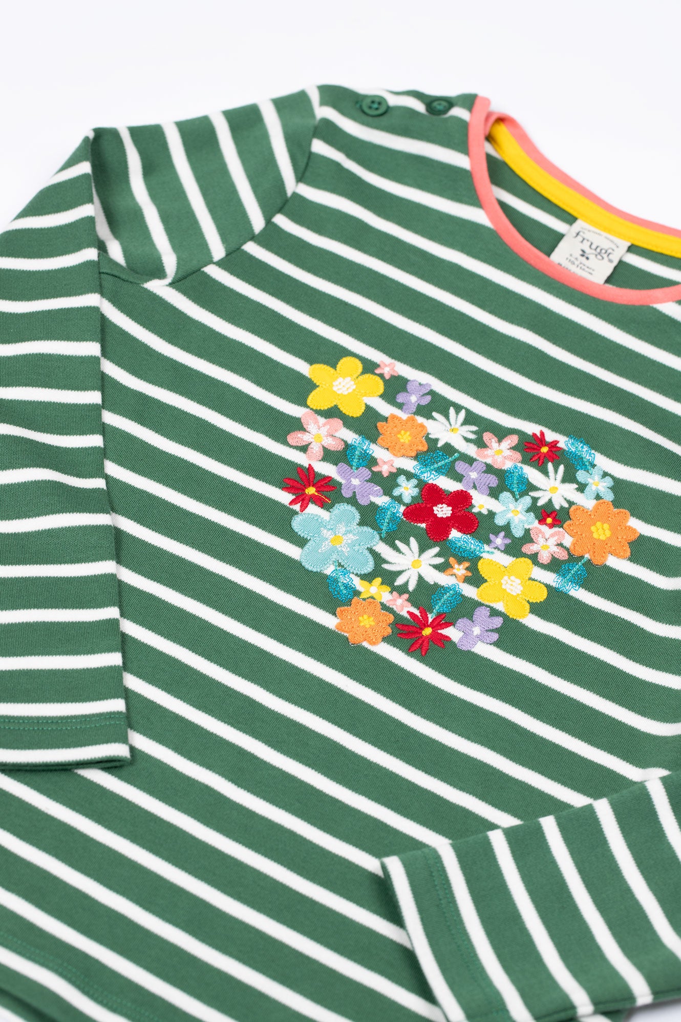 Close up of folded sleeves and flower appliqués and embroidery detailing on GOTS organic cotton top