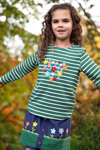 Girl wearing green and white striped organic cotton top with flower appliqués and embroidery detailing and pink neckline