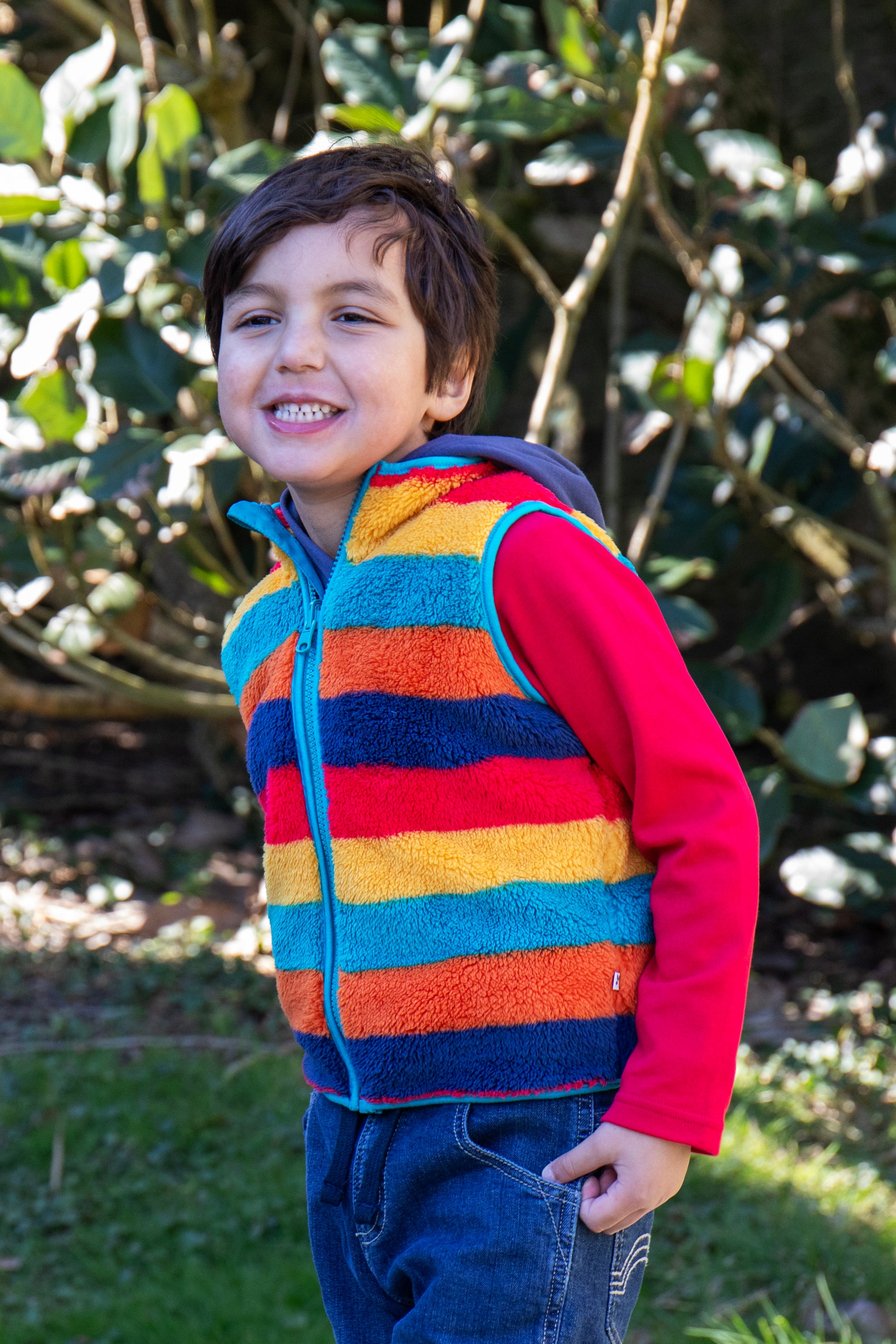 Child wearing a colorful striped vest and red shirt outdoors