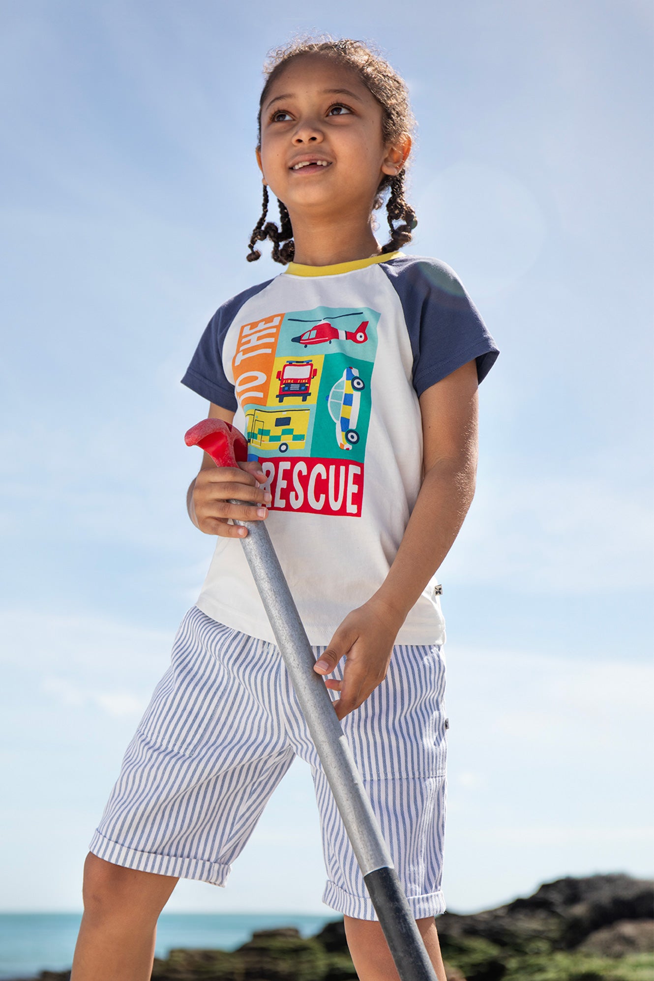 Child wearing the Frugi Reid Raglan T-Shirt in Soft White/Rescue, smiling outdoors in a natural setting.