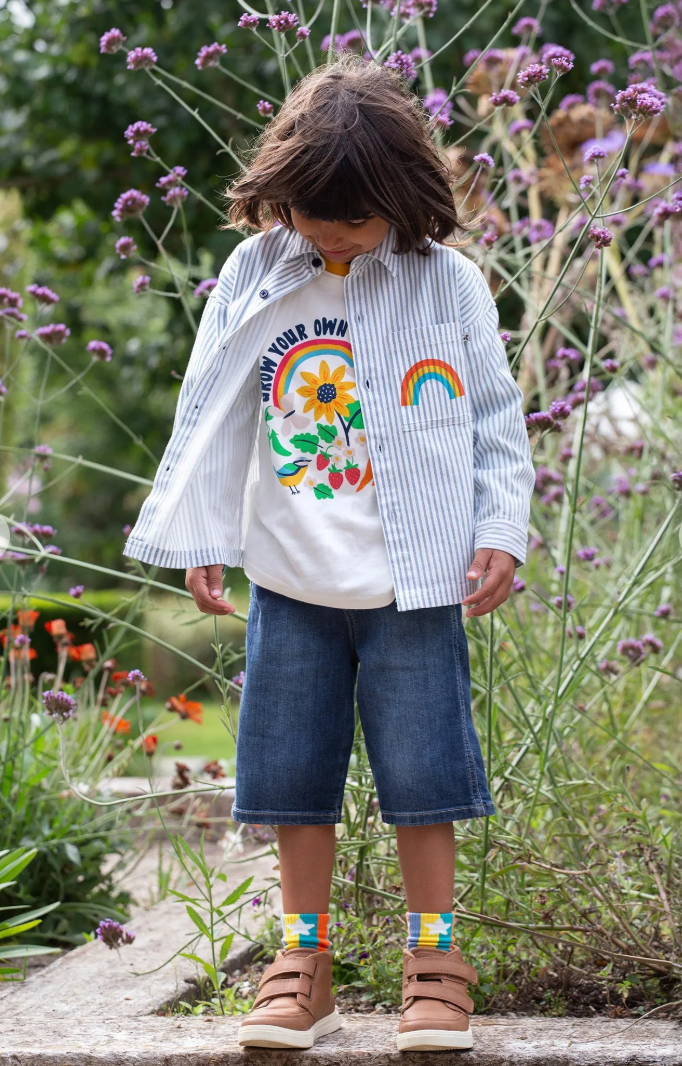 Child wearing the Frugi Tamar Raglan Top in Soft White/Grow Your Own Way, smiling outdoors in a natural setting.