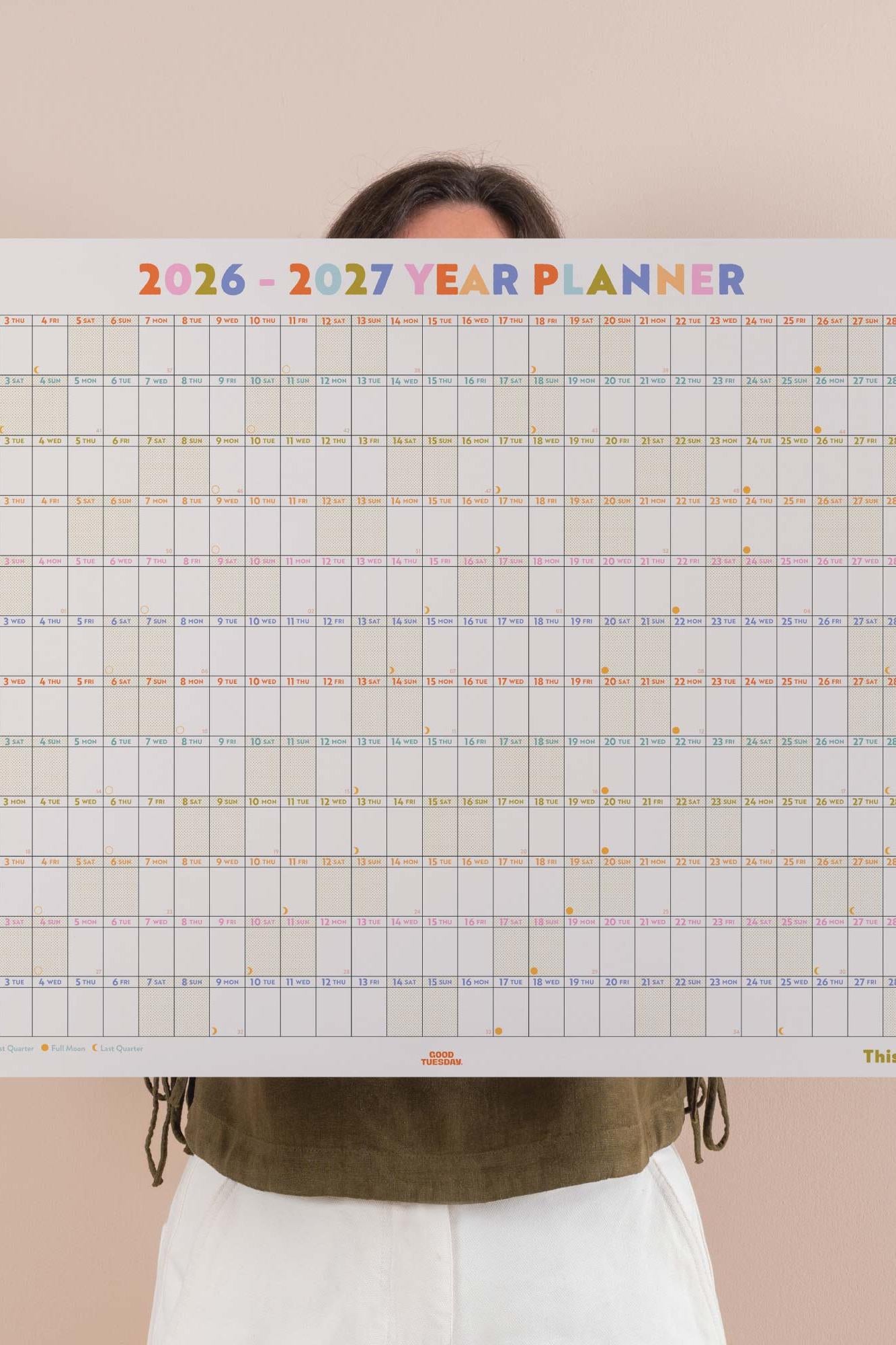 Person holding a 2026-2027 year planner against a beige background