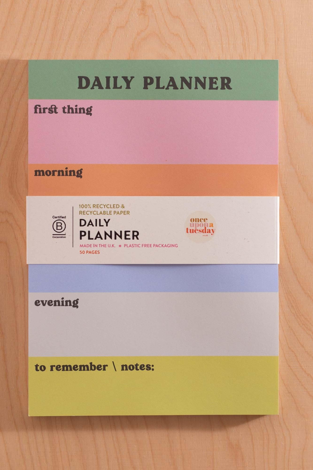 Colourful daily planner with sections for different times of the day on a wooden surface and B Corp logo.