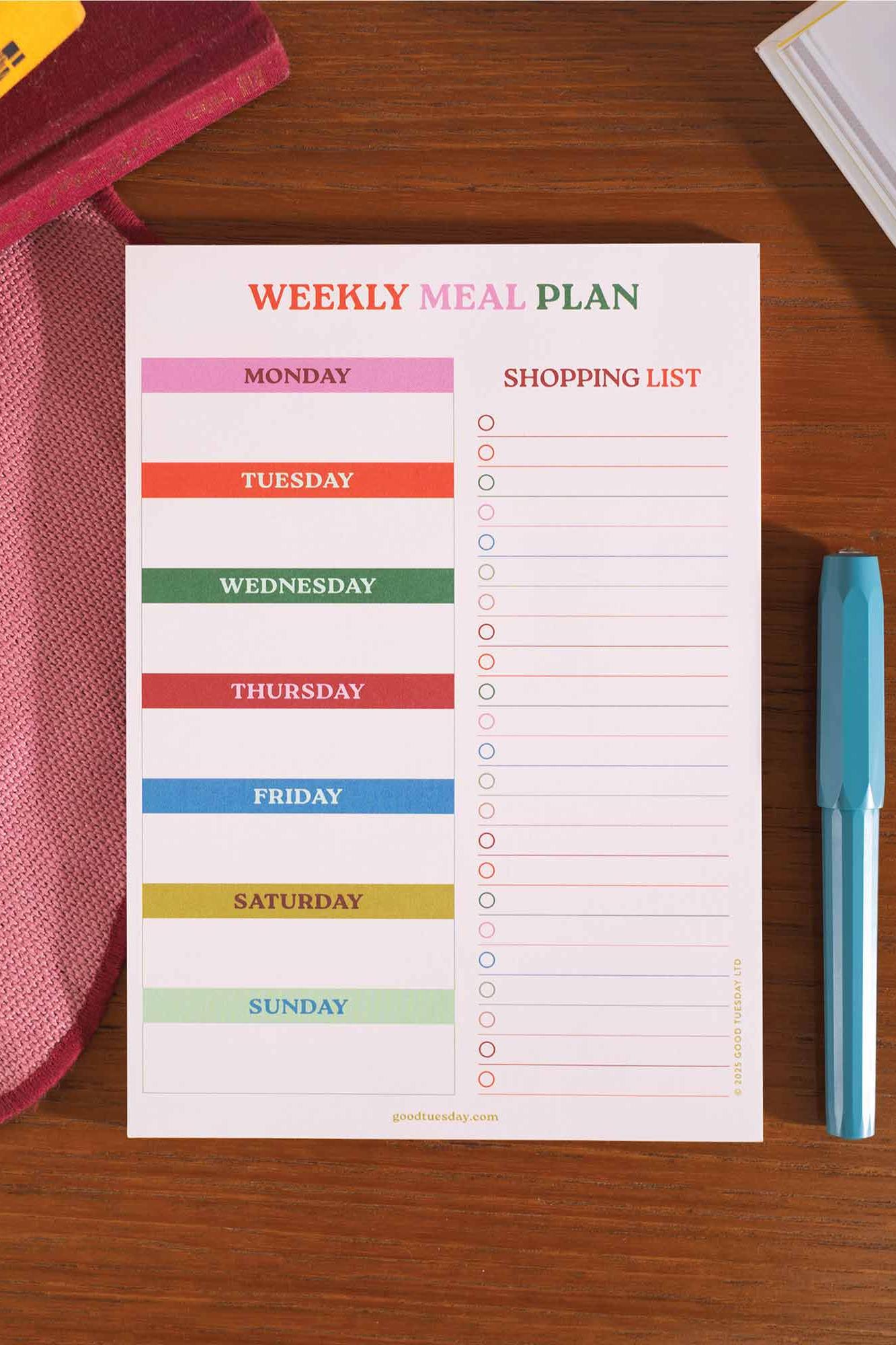 Weekly meal plan and shopping list on a wooden surface with a pen.
