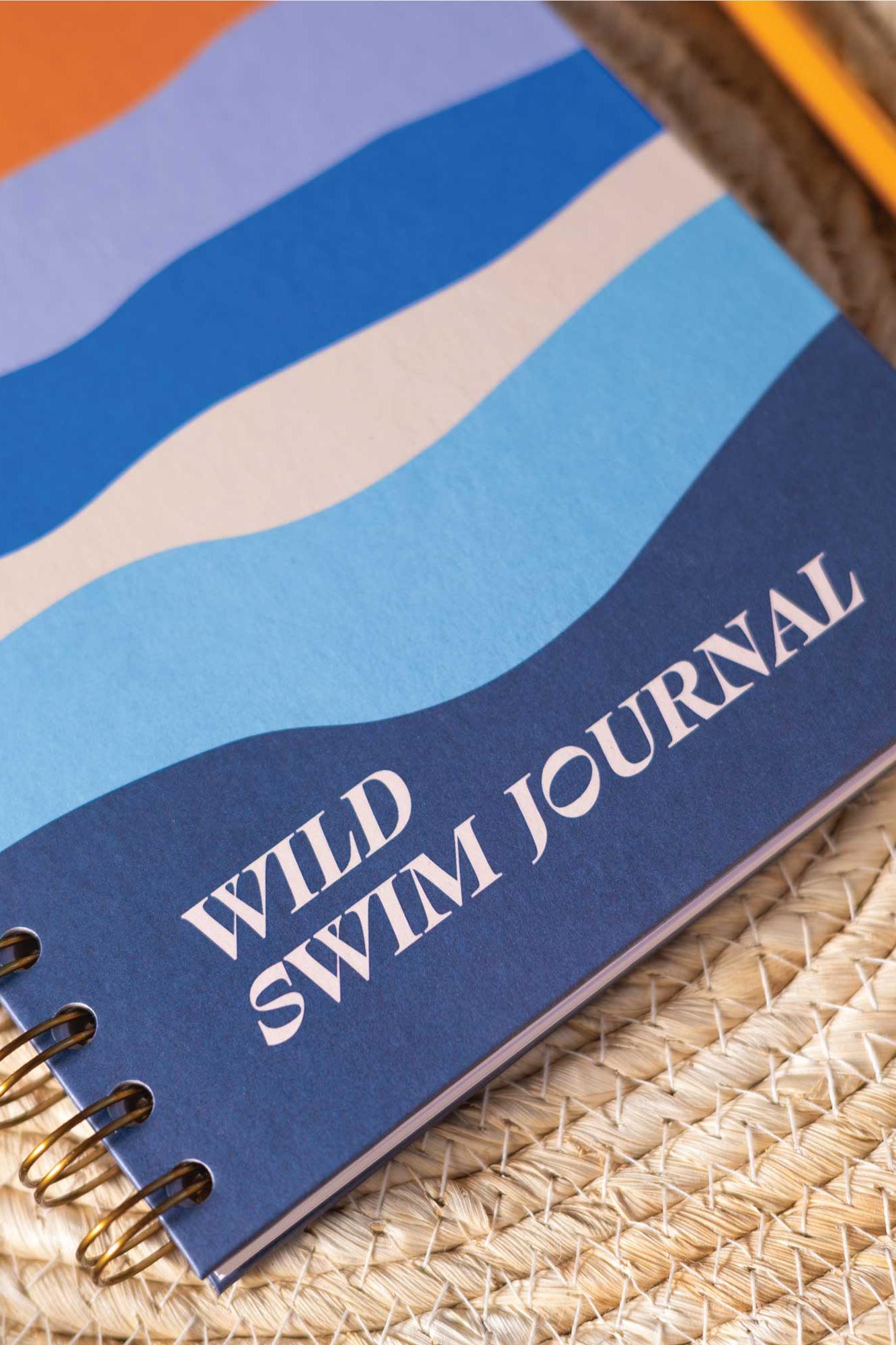 Notebook titled 'Wild Swim Journal' on a woven surface