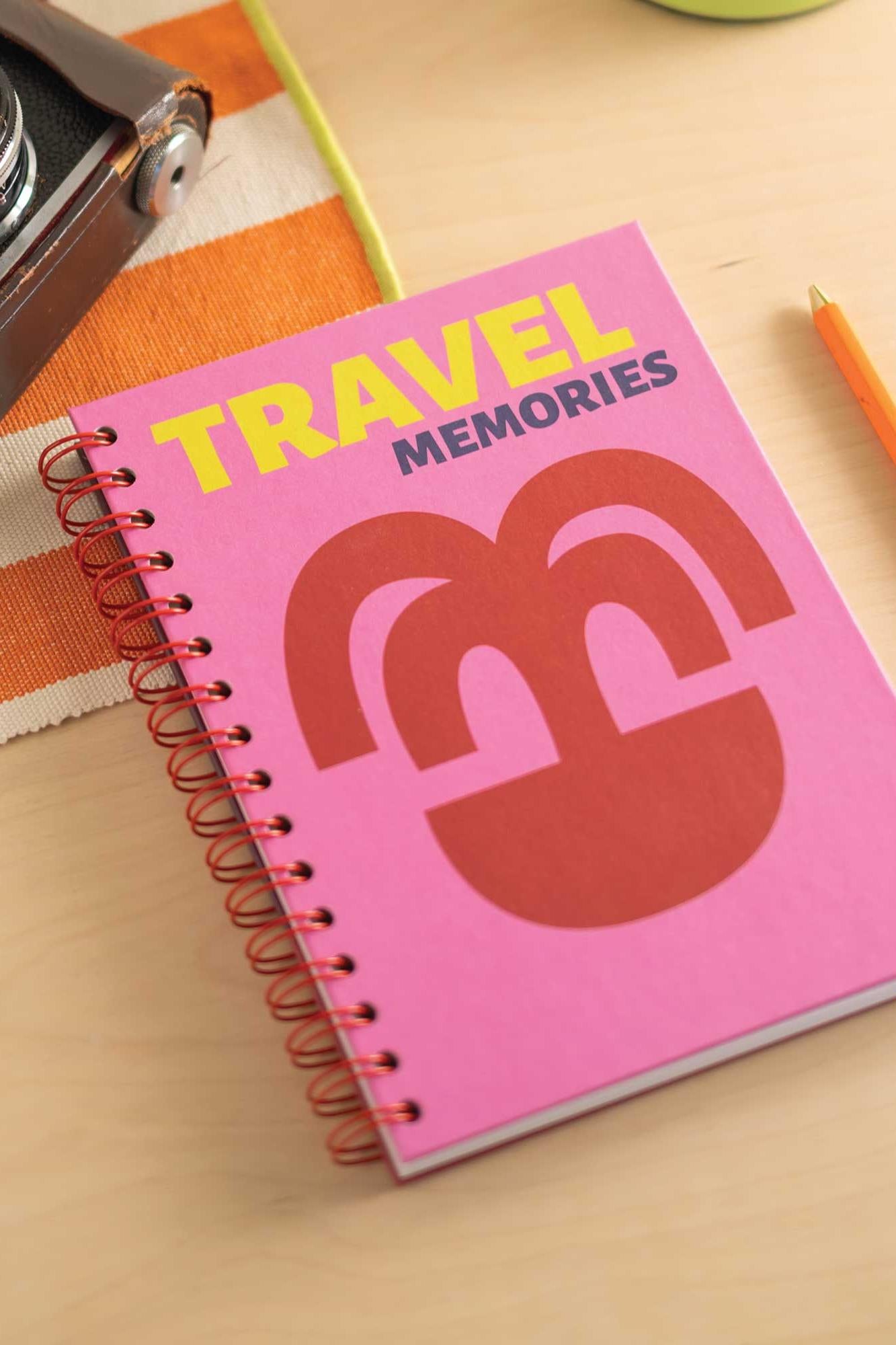 Pink notebook titled 'Travel Memories' on a wooden surface with a camera and pen.