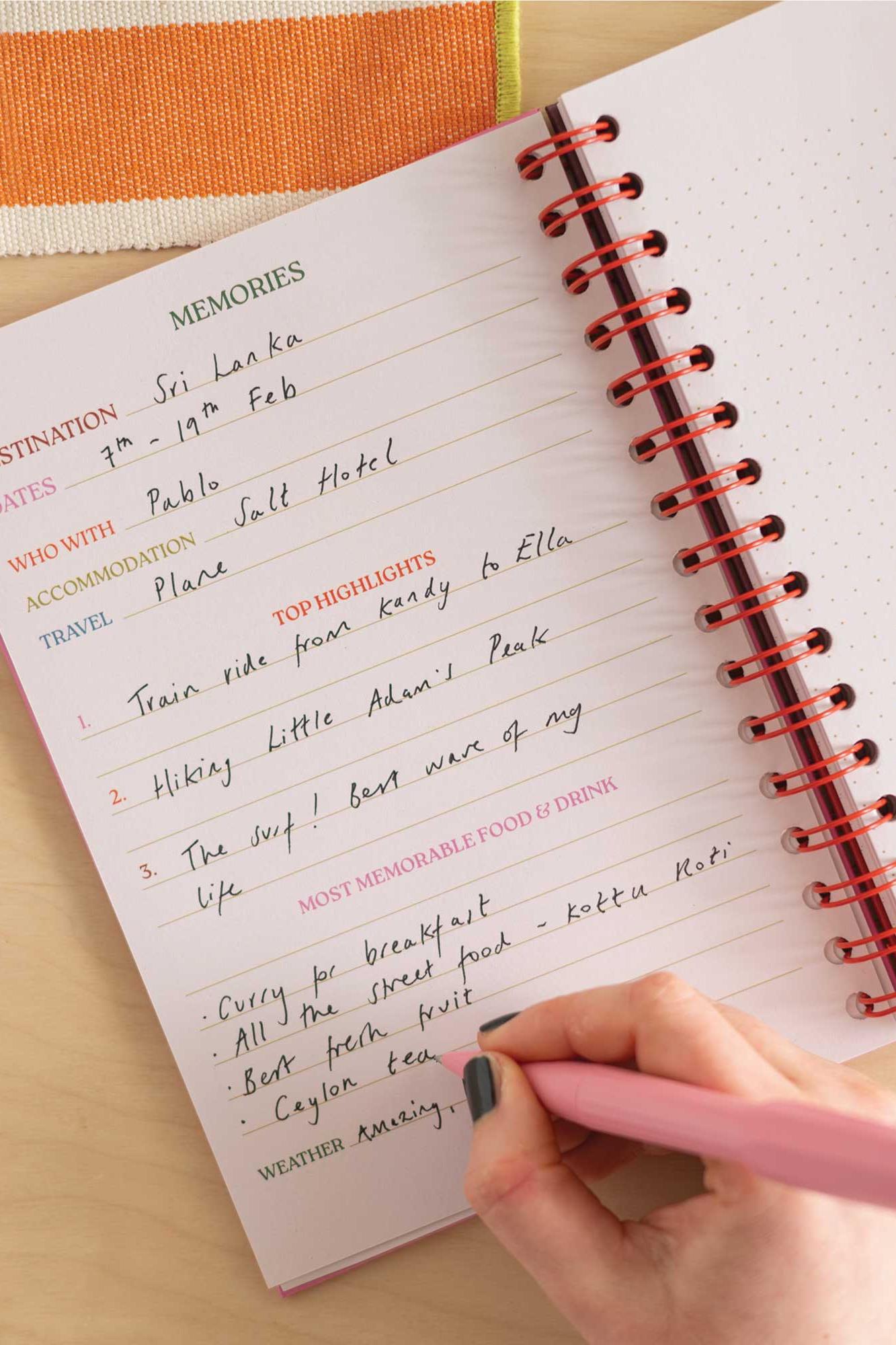 Person writing in a travel journal on a wooden surface