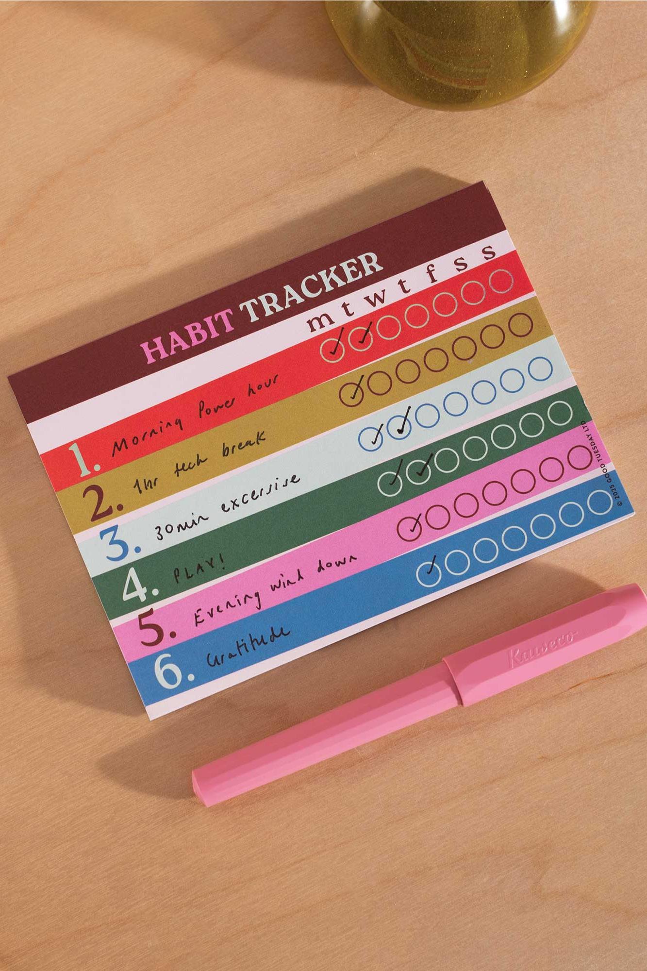 Colorful habit tracker with checkboxes on a wooden surface with a pink pen.