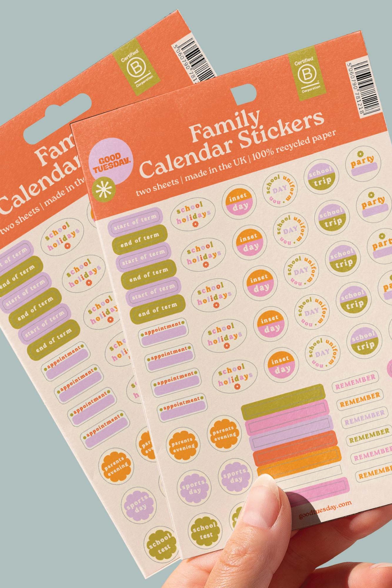Family calendar stickers with colourful designs held by a hand against a gray background