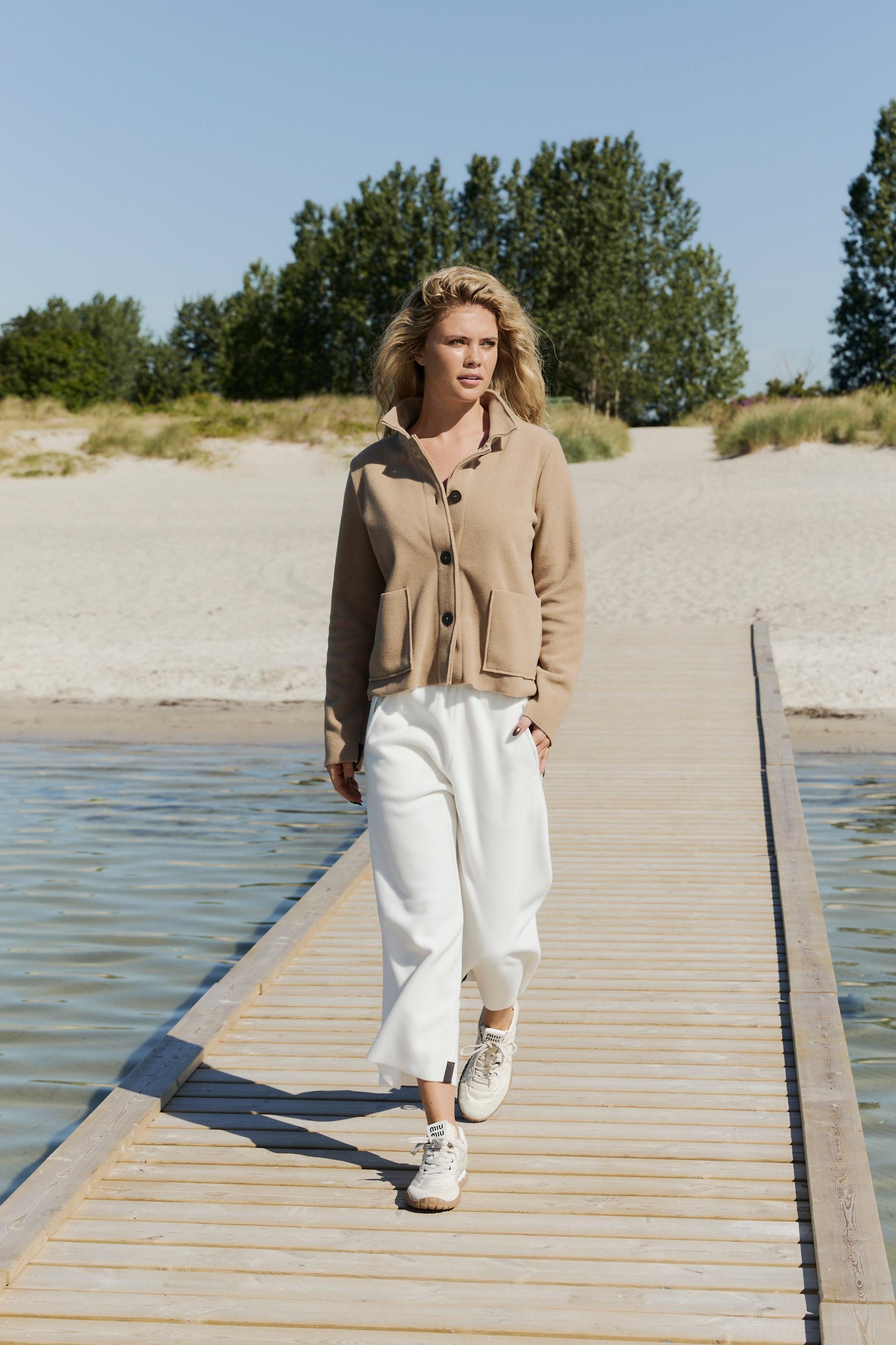 Woman walking on a wooden dock by a body of water with trees in the background