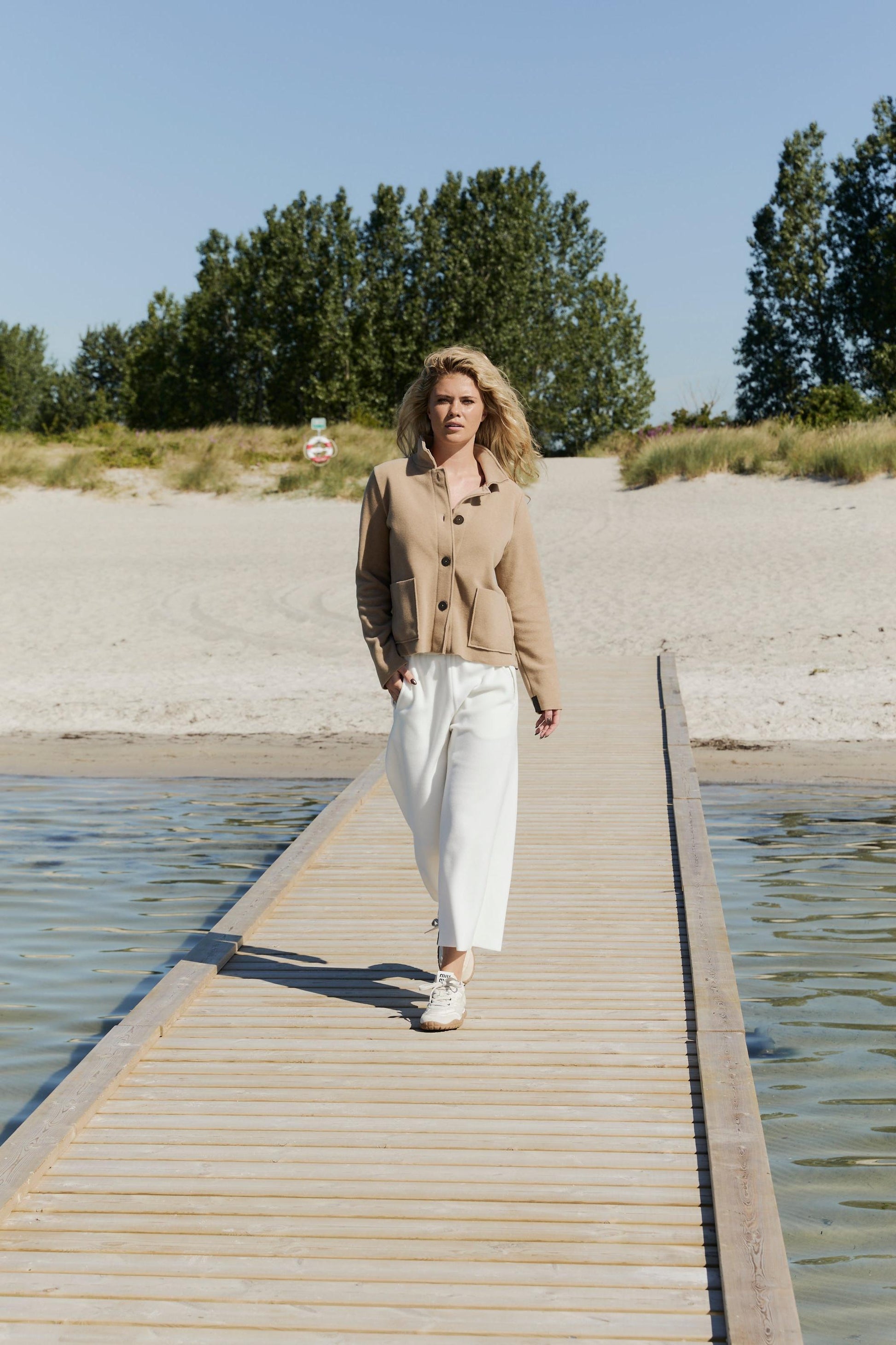 Woman walking on a wooden dock by a body of water wearing a Henriette Steffensen fleece jacket