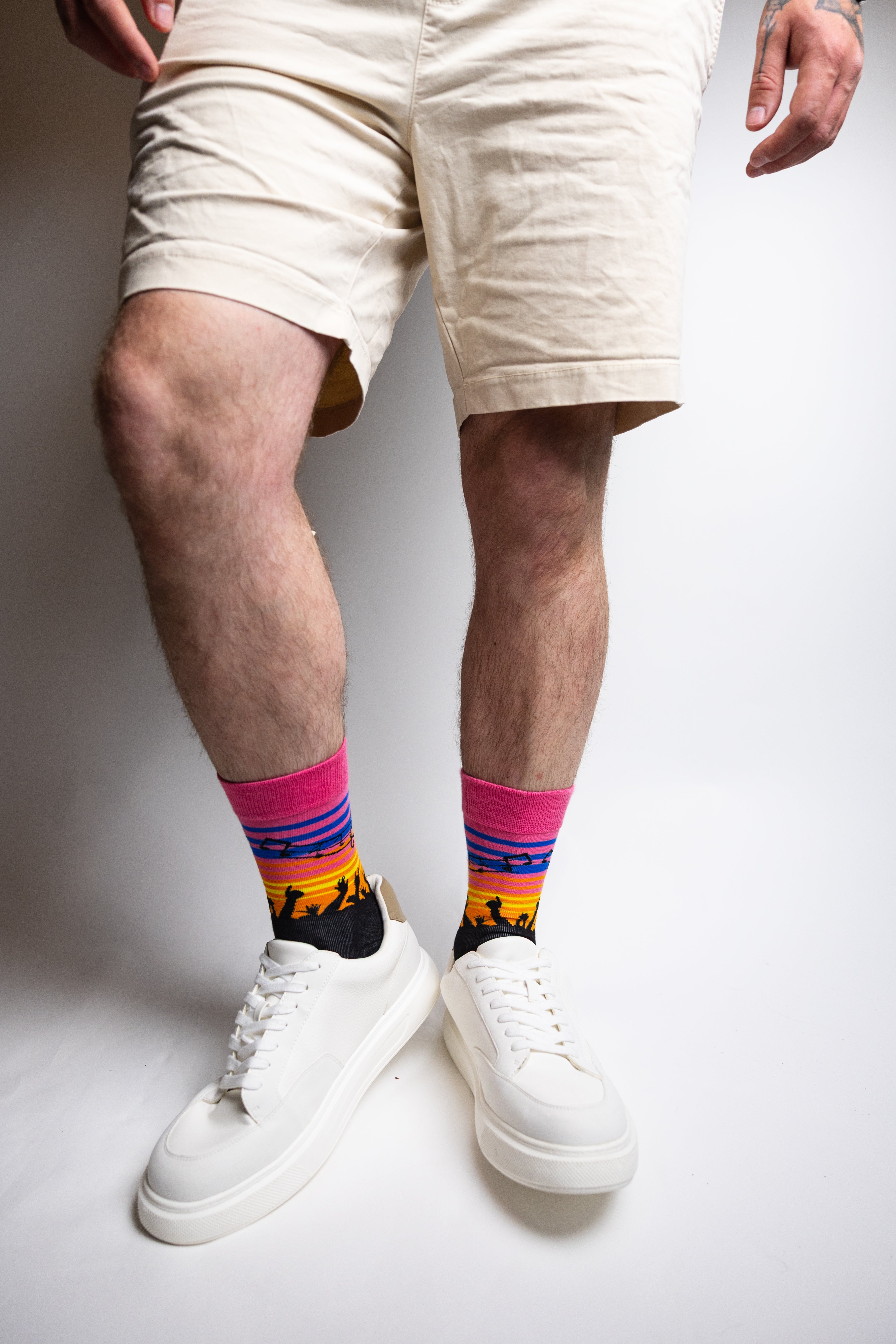Person wearing colorful socks with a mountain design, white sneakers, and beige shorts on a plain background.