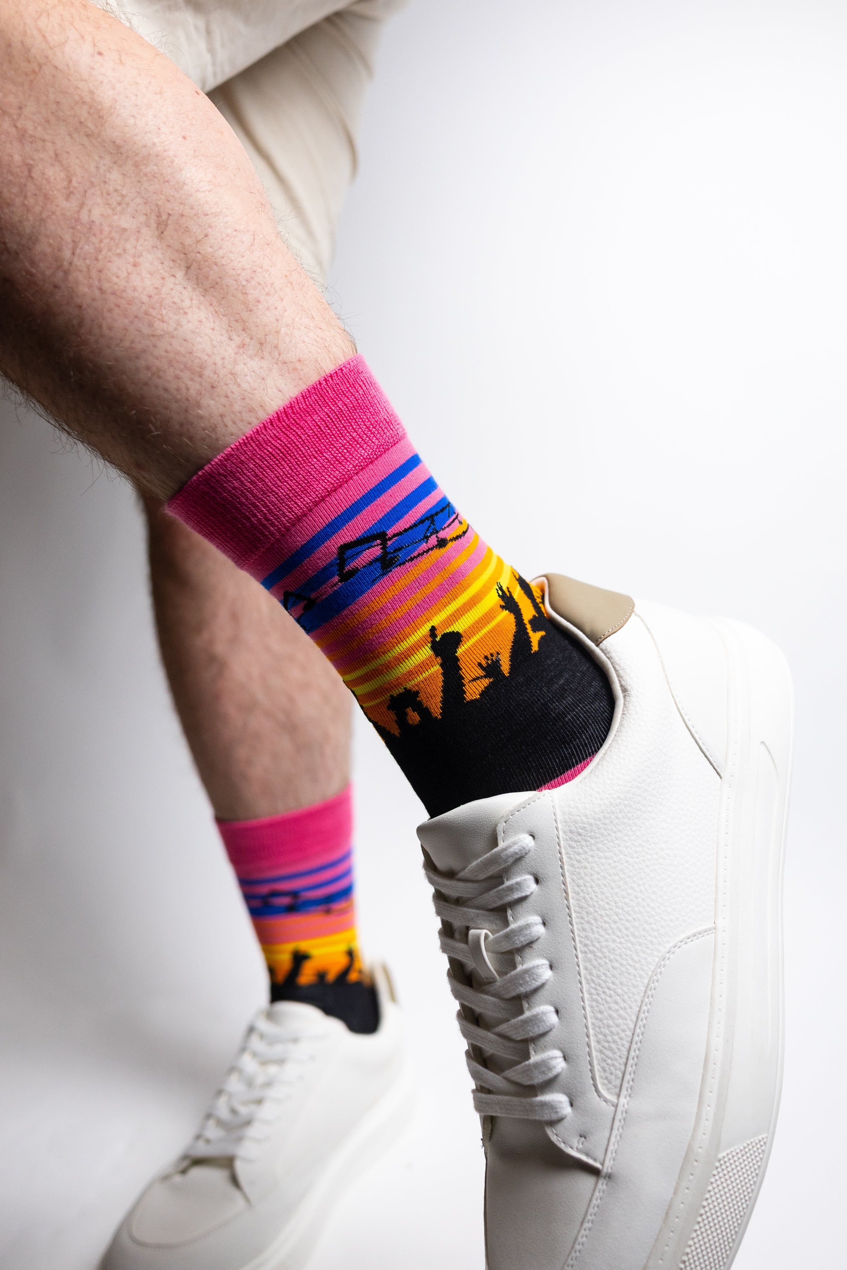 Colorful socks with a design of people dancing worn with white sneakers on a light background