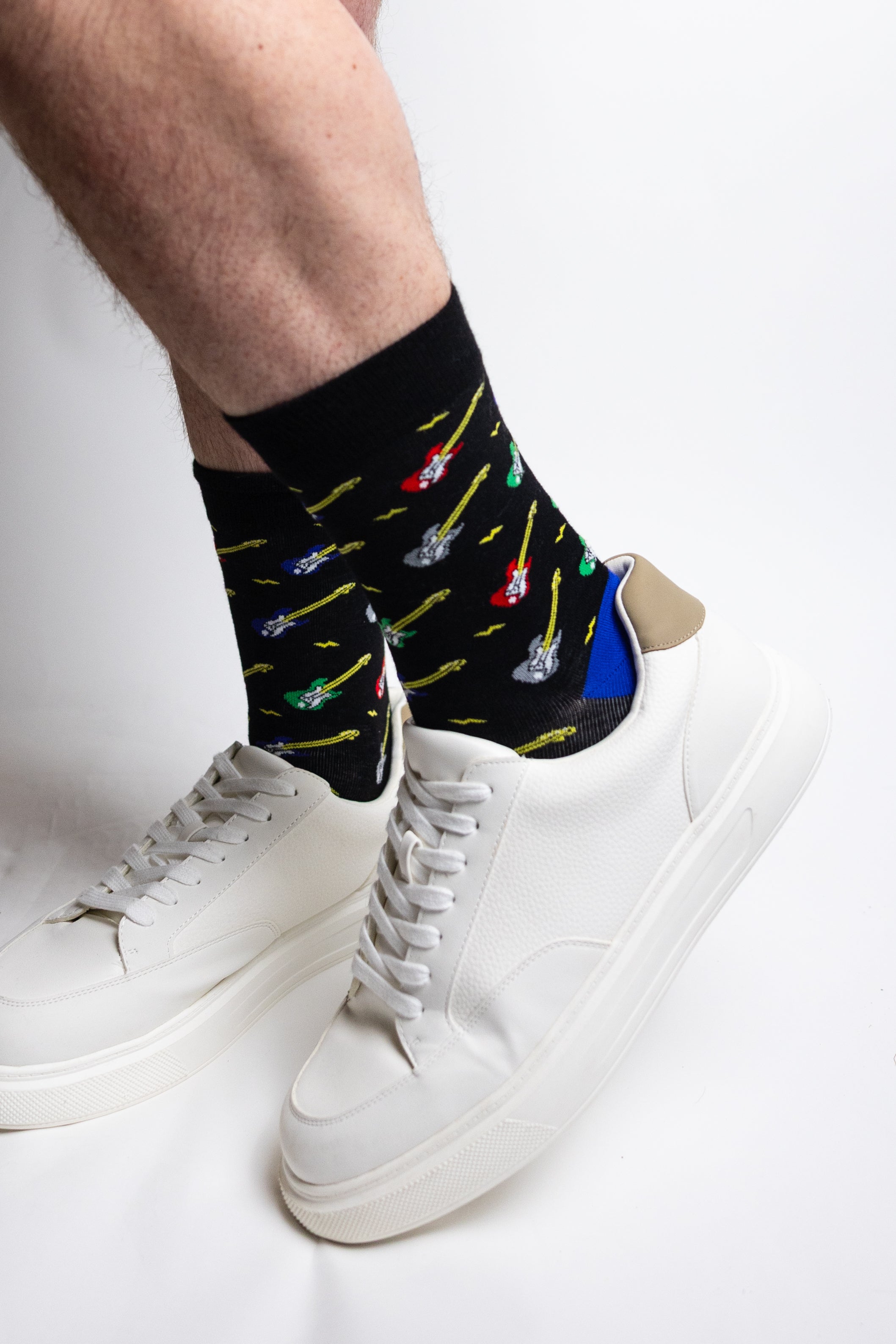 Man wearing black bamboo socks with electric guitar print and white trainers on light background