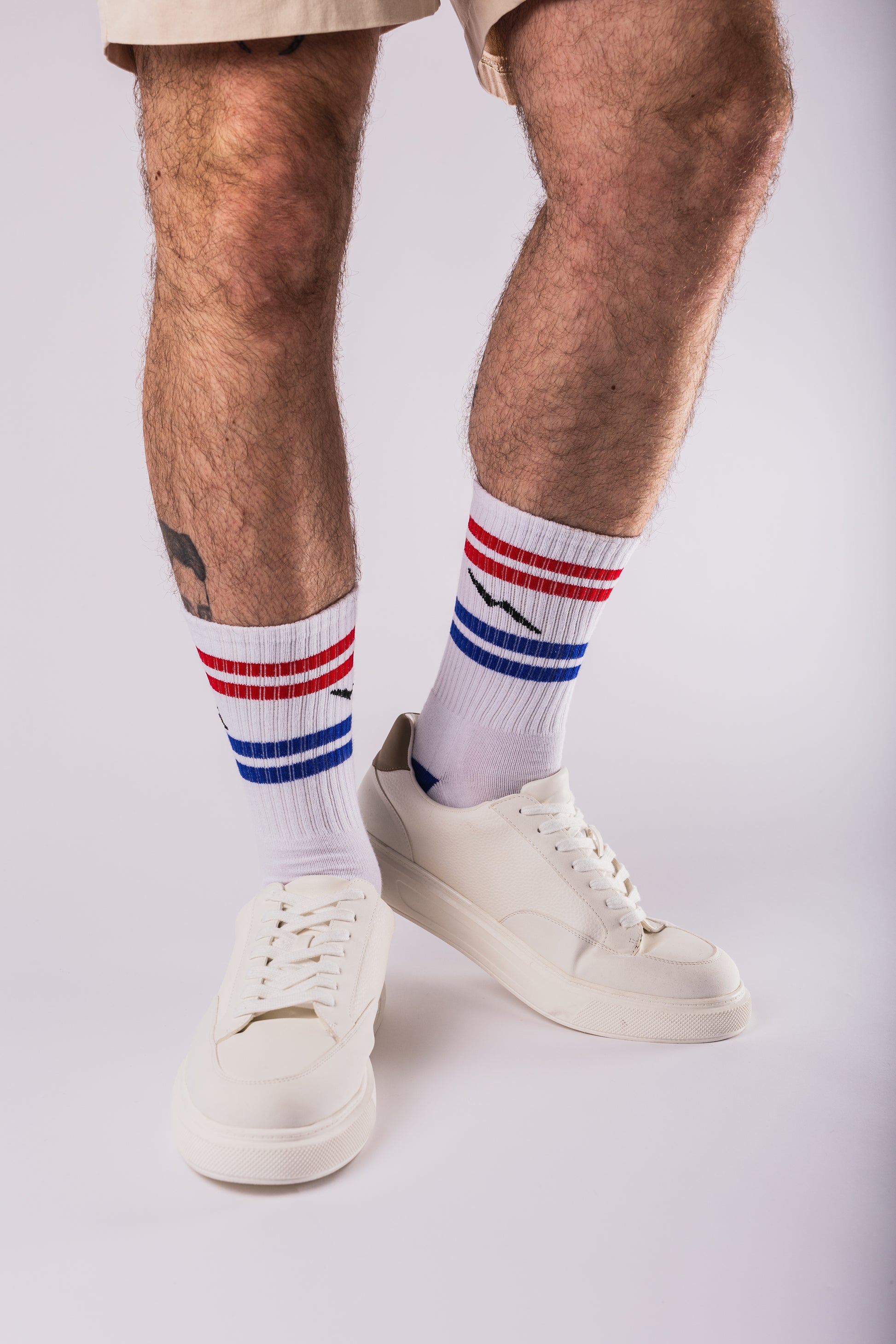 Person wearing white socks with red, blue, and white stripes and white sneakers on a light gray background