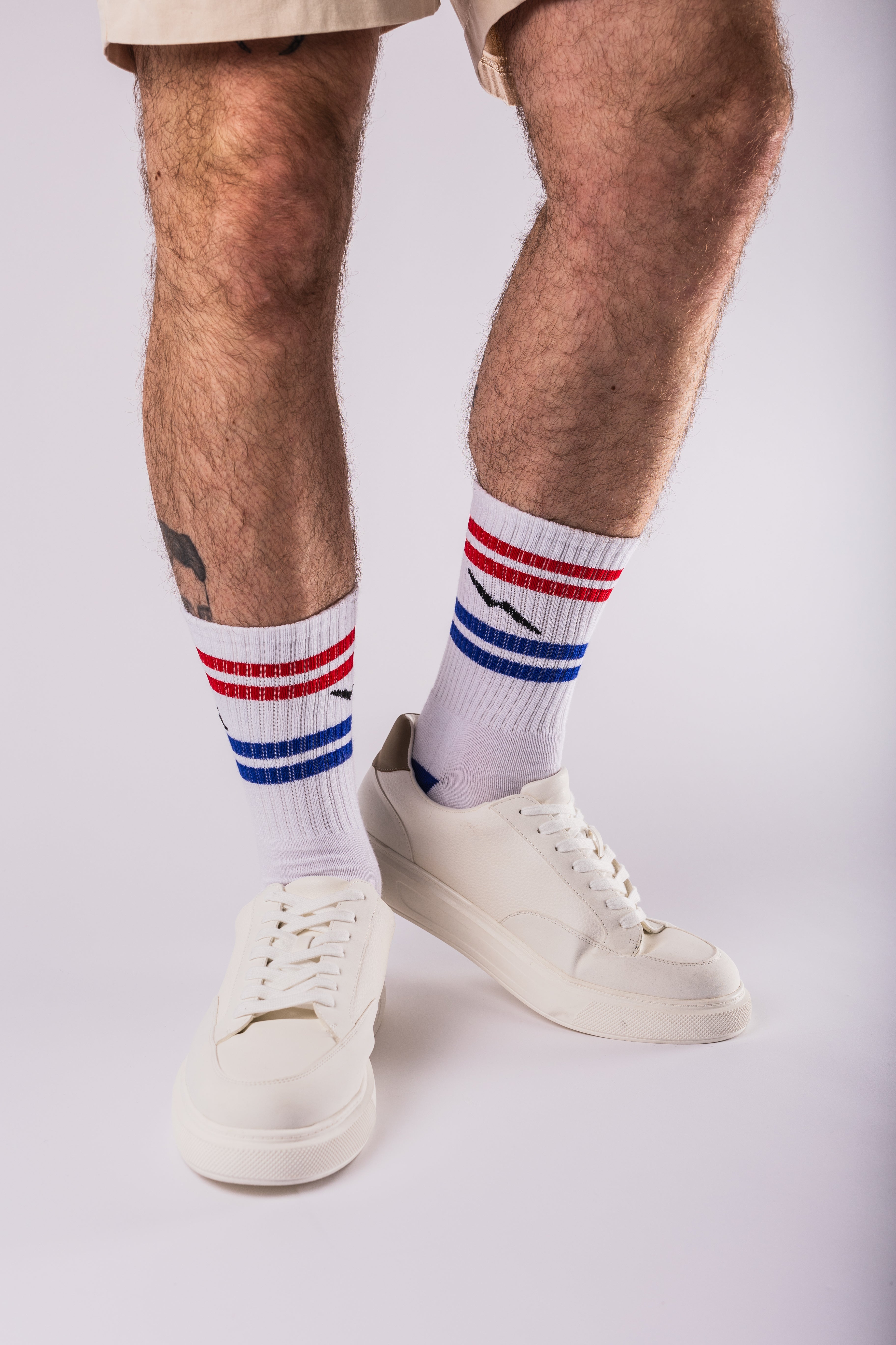 Person wearing white socks with red, blue, and white stripes and white sneakers on a light gray background