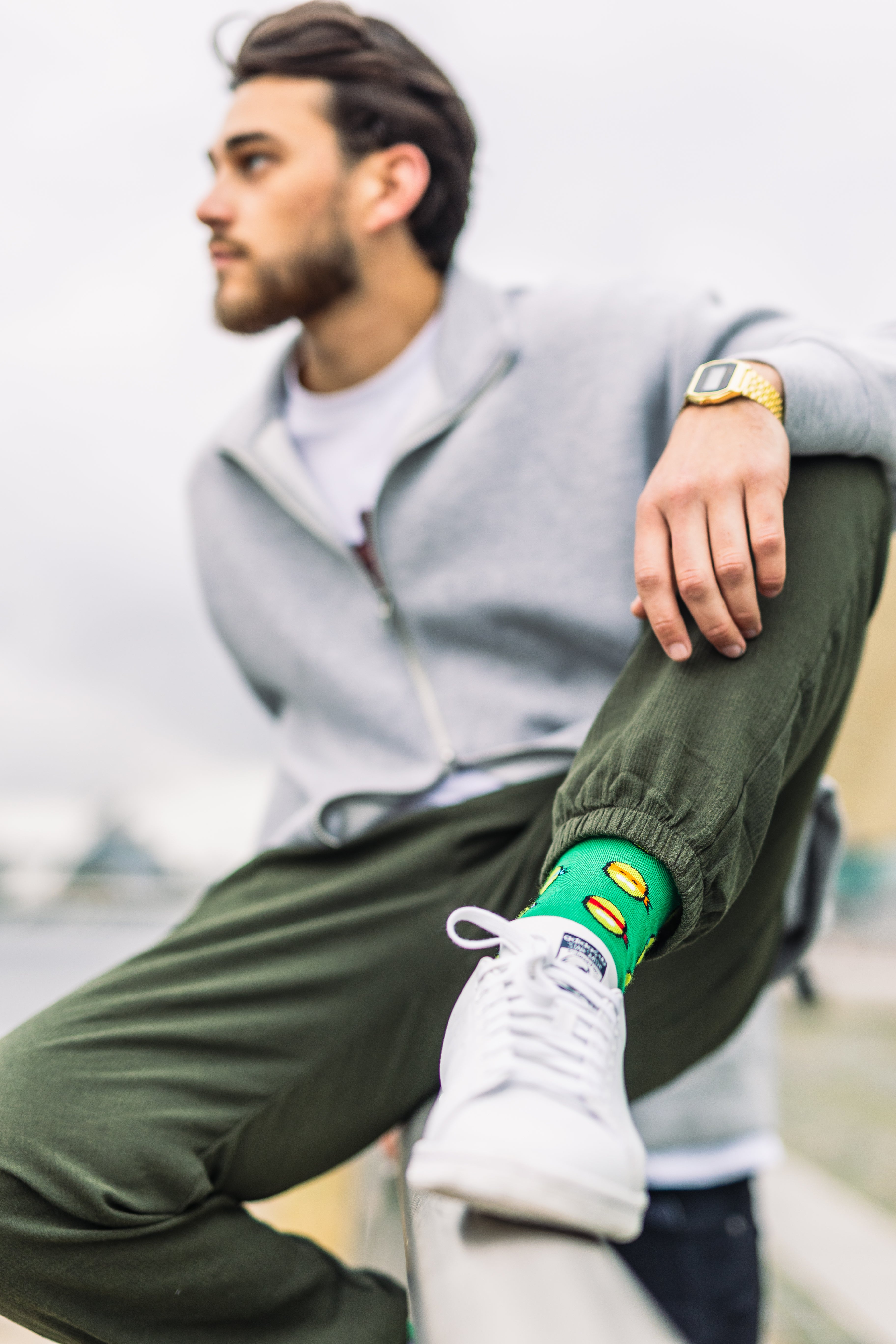 Man wearing a gray hoodie, green pants, and white sneakers with a colorful sole.