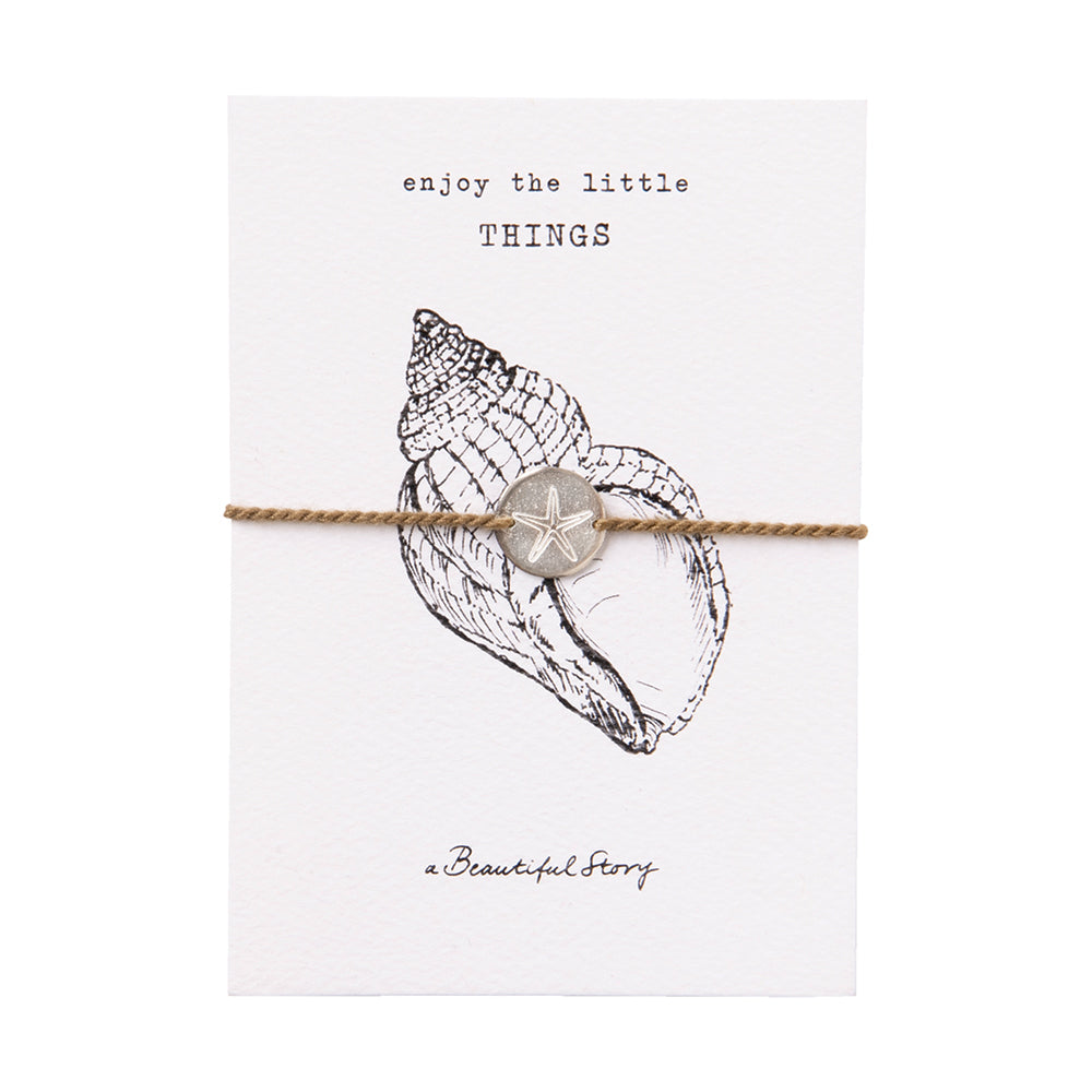 A shell bracelet on a card with writing "enjoy the little things" and branding