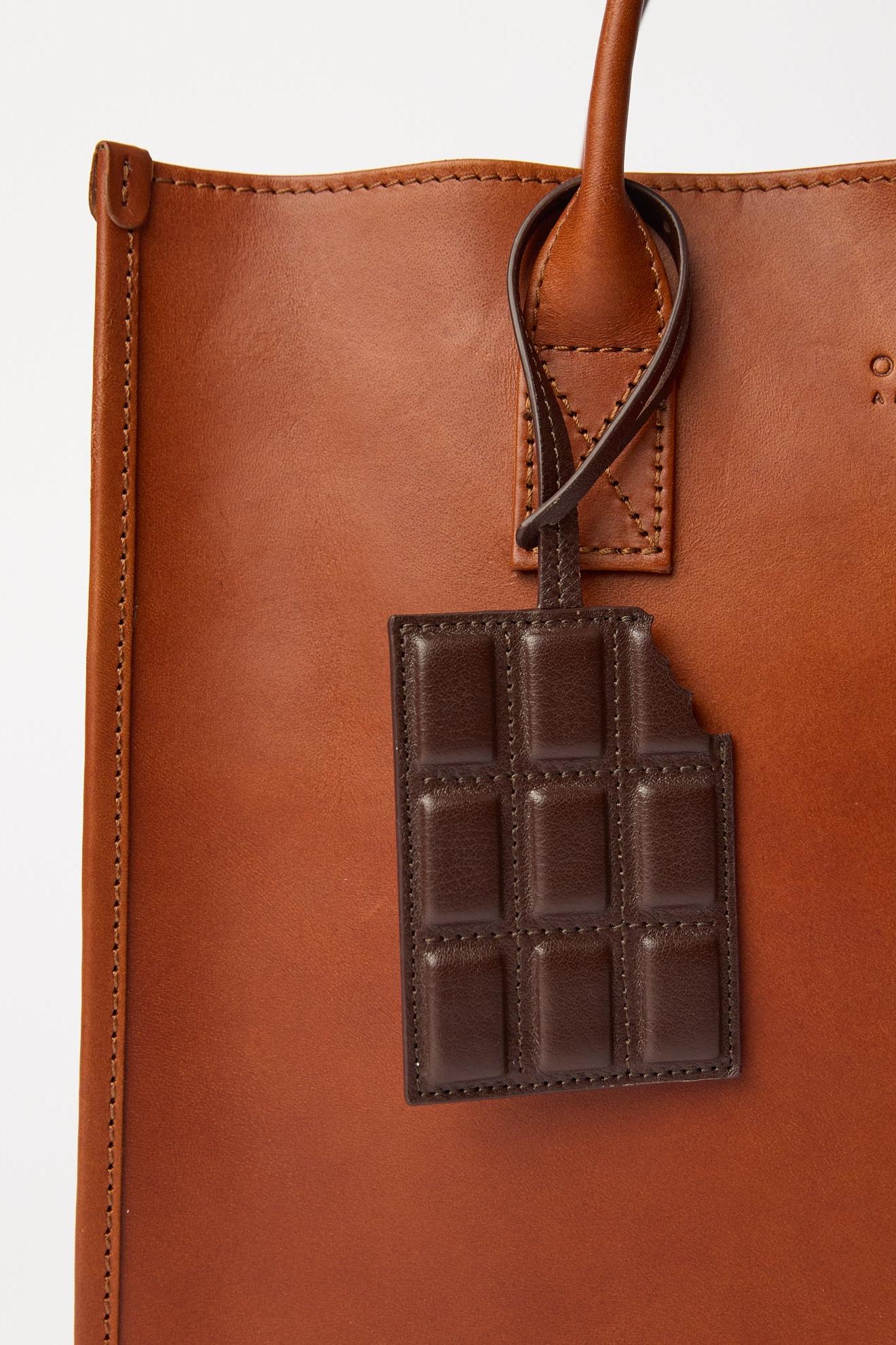 Brown leather bag with a chocolate bar-shaped tag on a white background