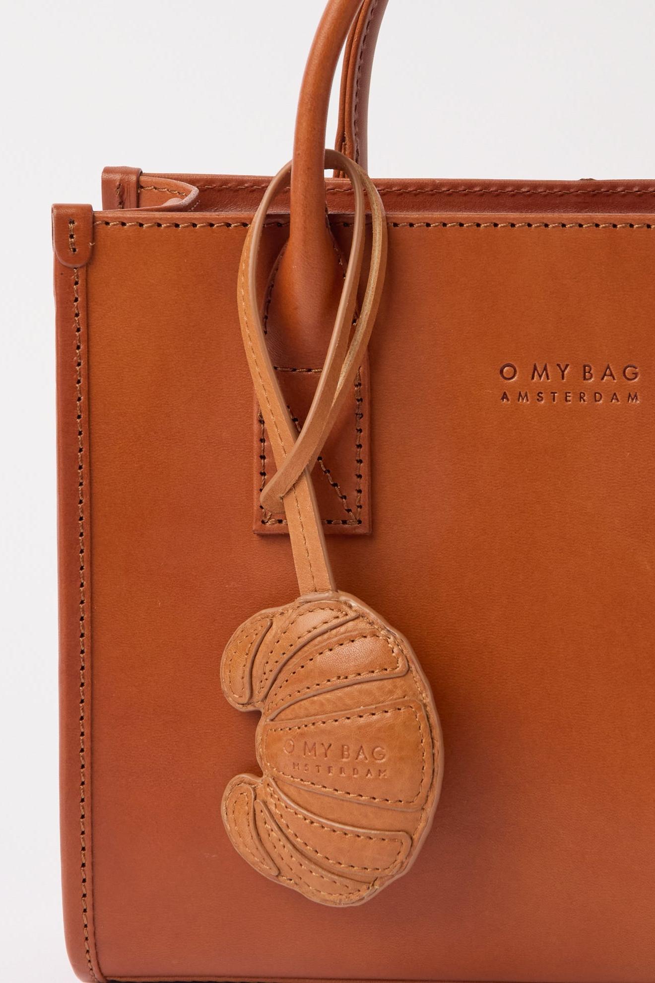 Brown leather bag with a decorative charm featuring 'O MY BAG' branding on a white background.