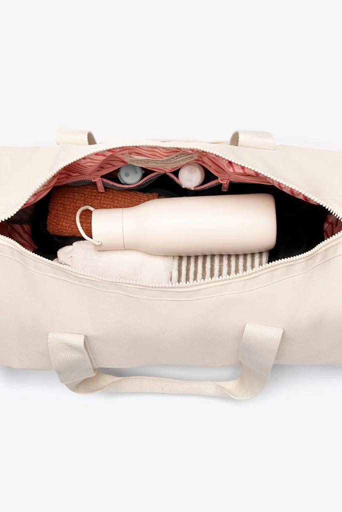 Overhead view of open duffle bag with bottle and clothing inside and show the two zipped pockets inside.