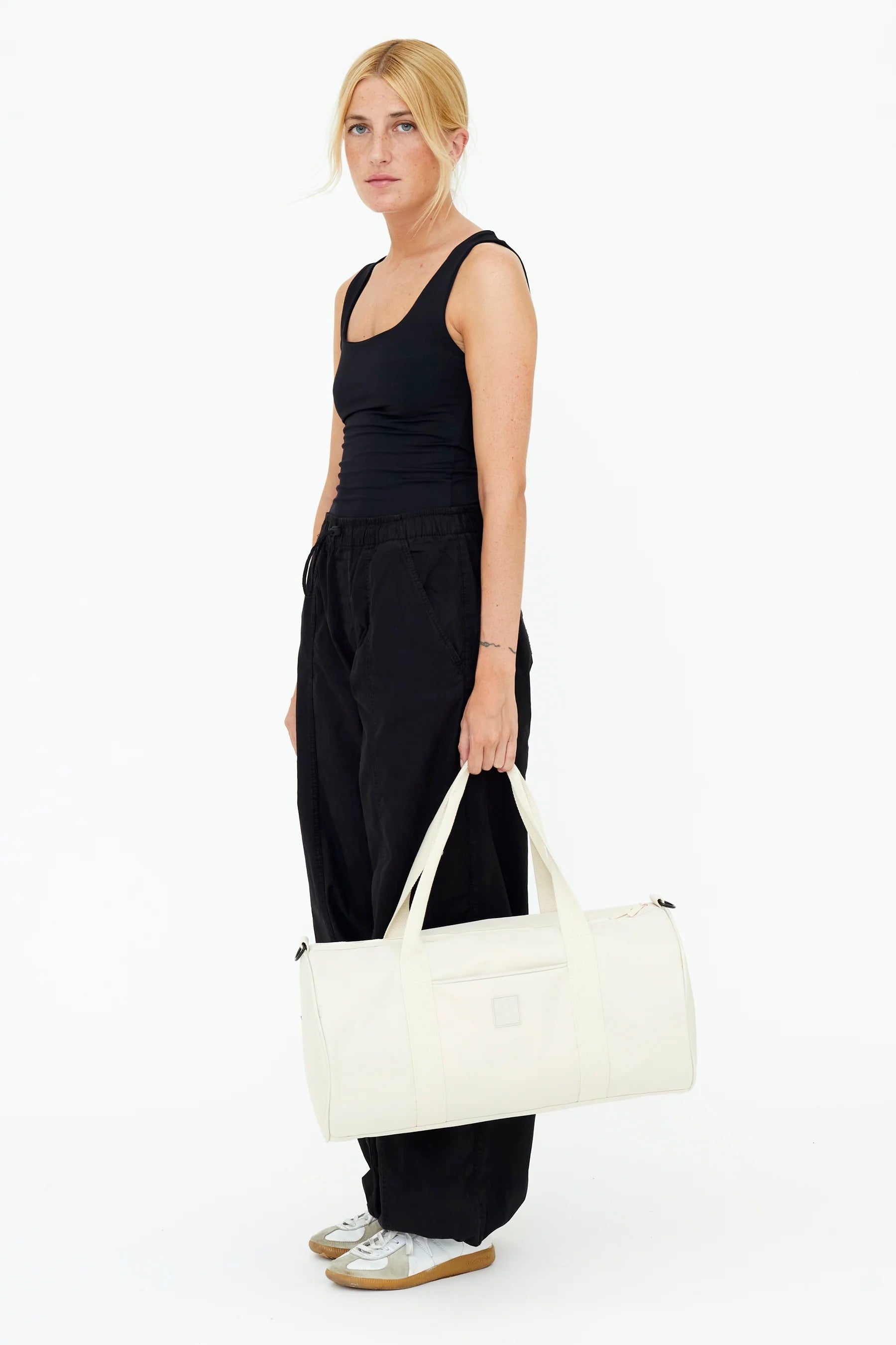 Model wearing all black holding the Lefrik Getaway bag by the straps by her legs.