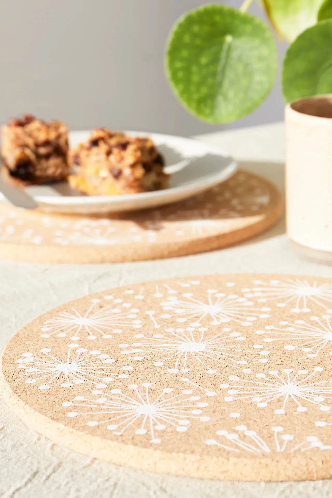 Lifestyle shot of Liga Cork Placemat featuring dandelion design, placed on a dining table with a plate of food.