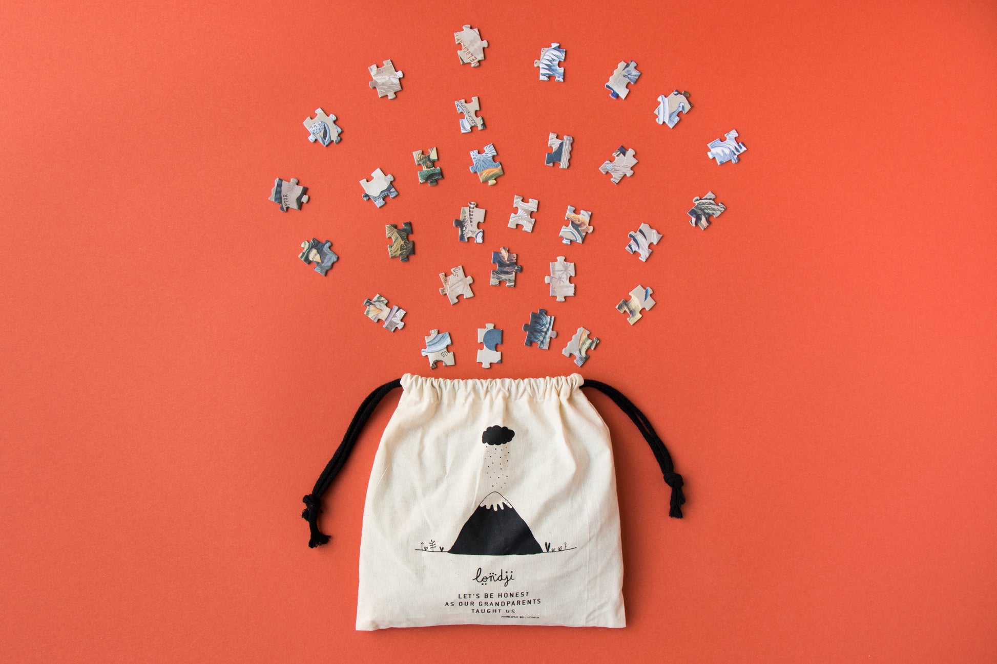 Drawstring bag with puzzle pieces spilling out on an orange background