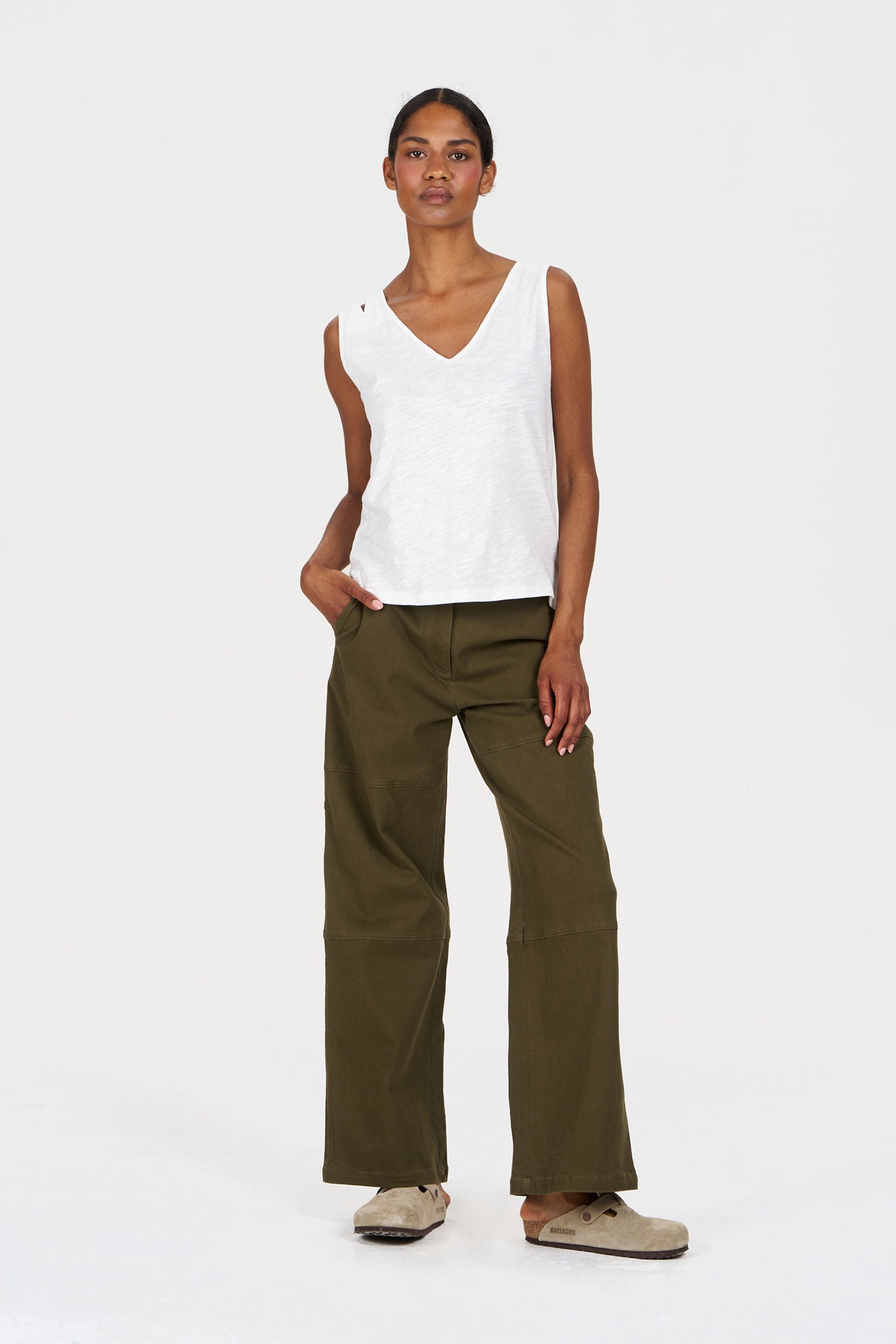 Woman wearing a white sleeveless top and olive green pants on a white background