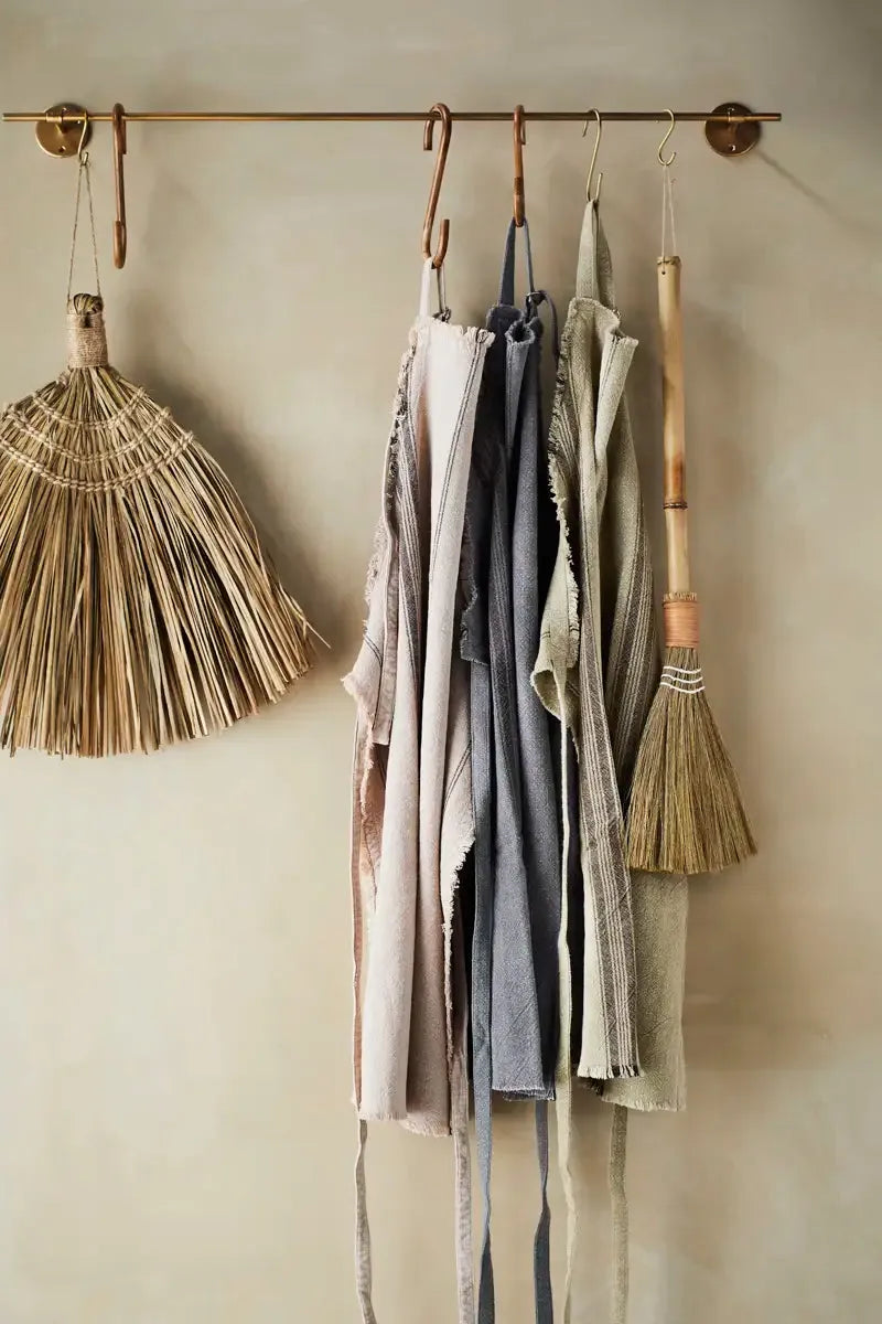 Set of aprons hanging on a rod with brooms on a neutral wall.