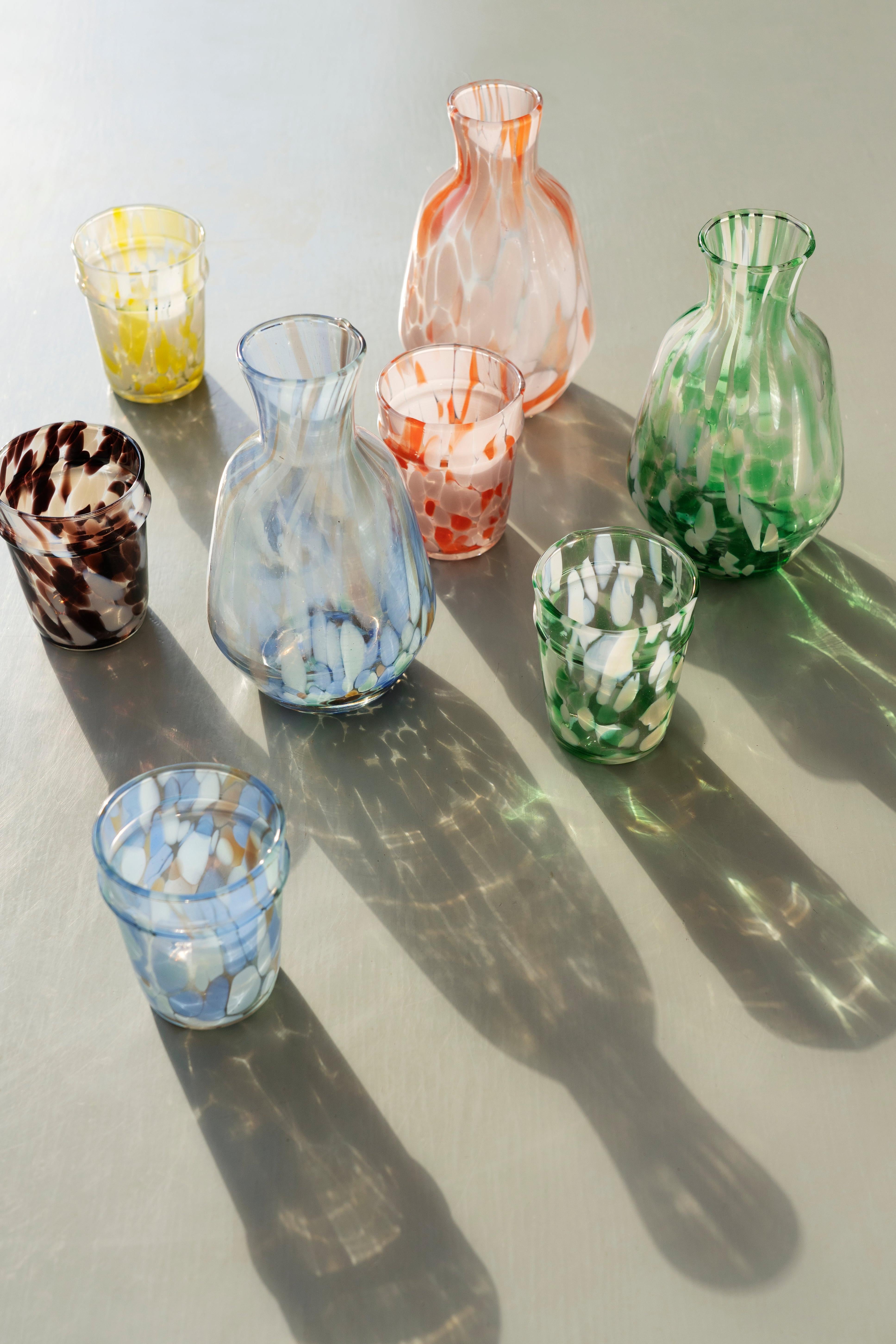 Collection of colorful glass vases and drinking glasses on a reflective surface