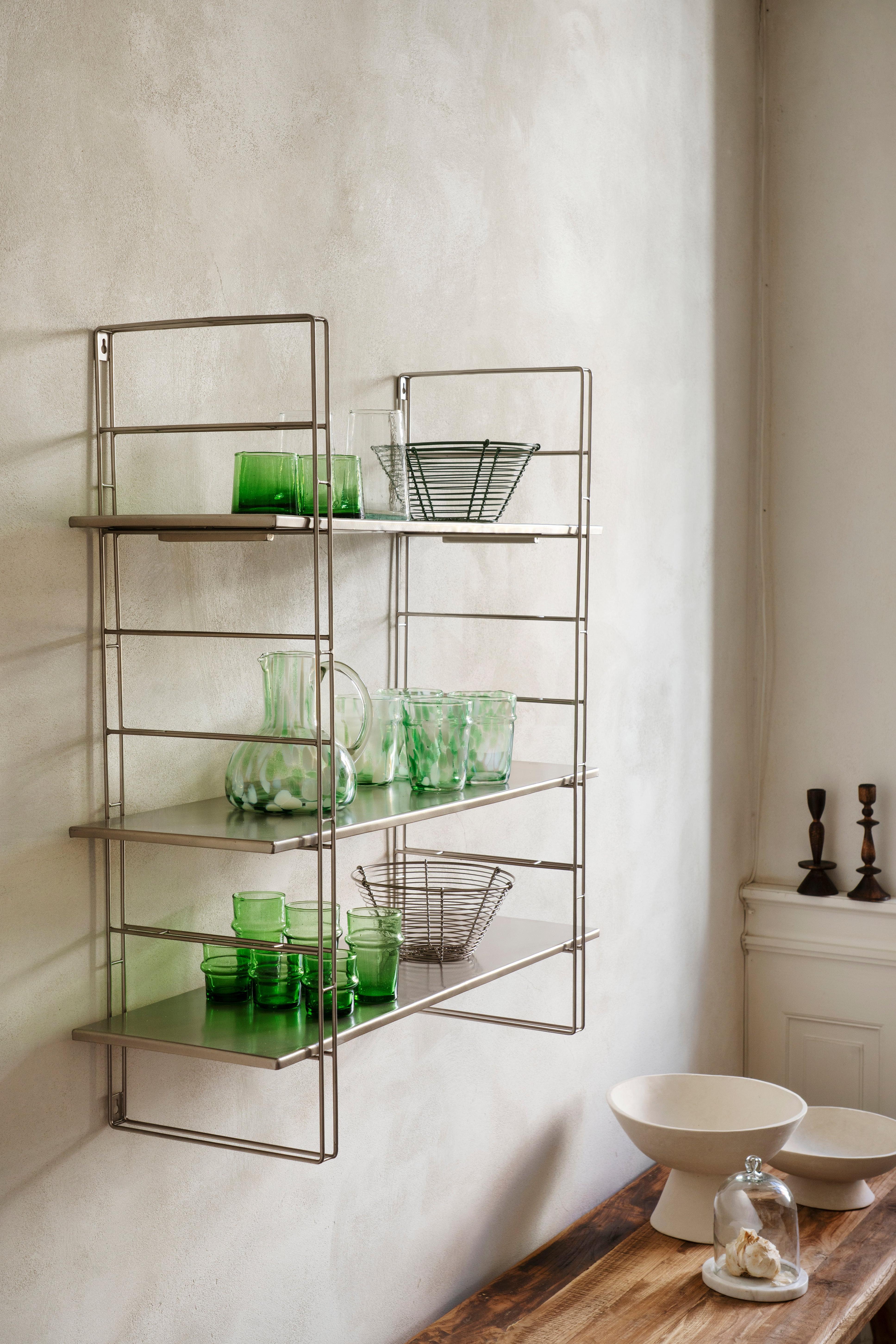 Metal wall shelf with green glassware against a white wall