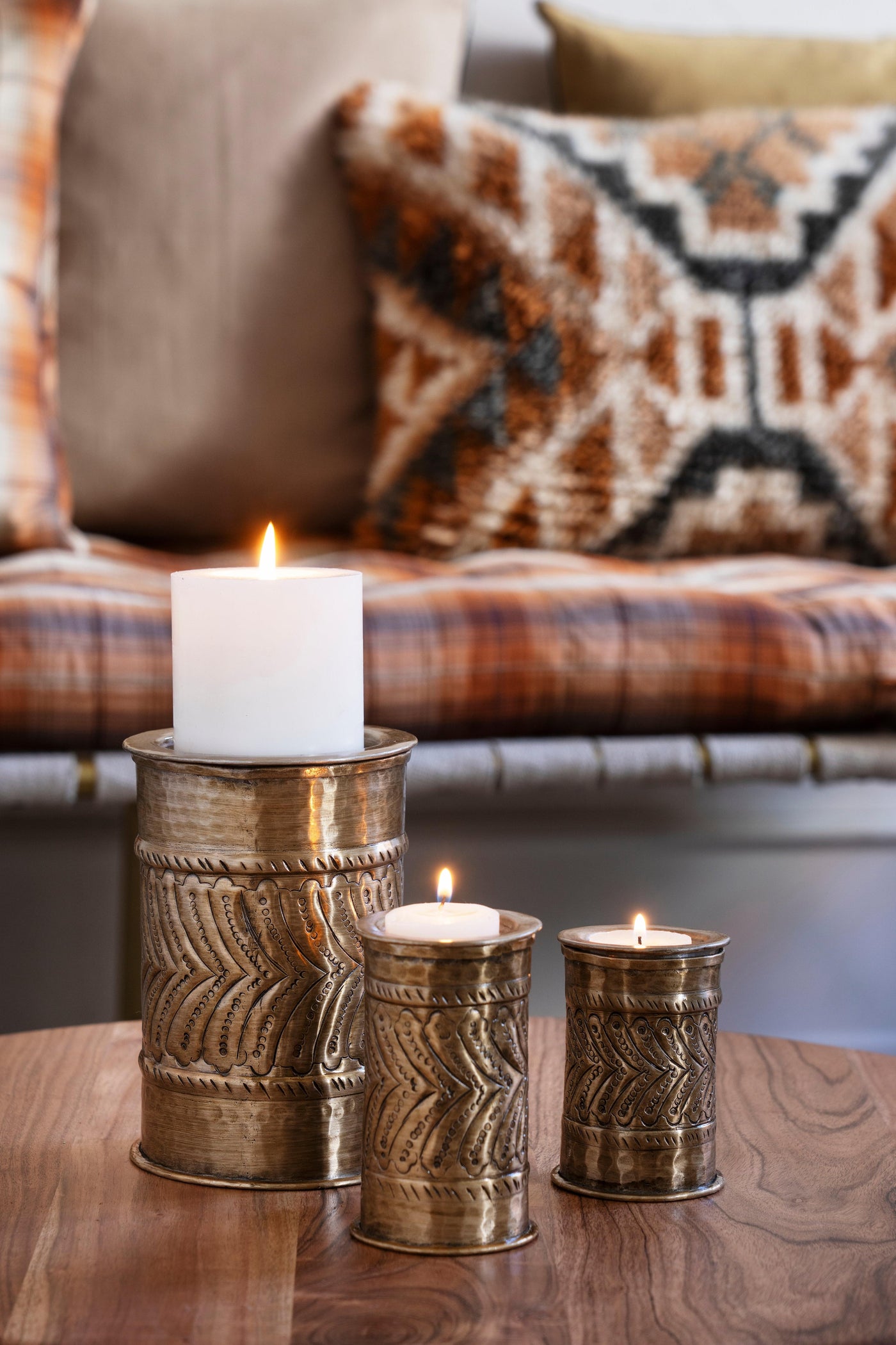Decorative candles in metallic holders on a wooden surface with a blurred sofa in the background