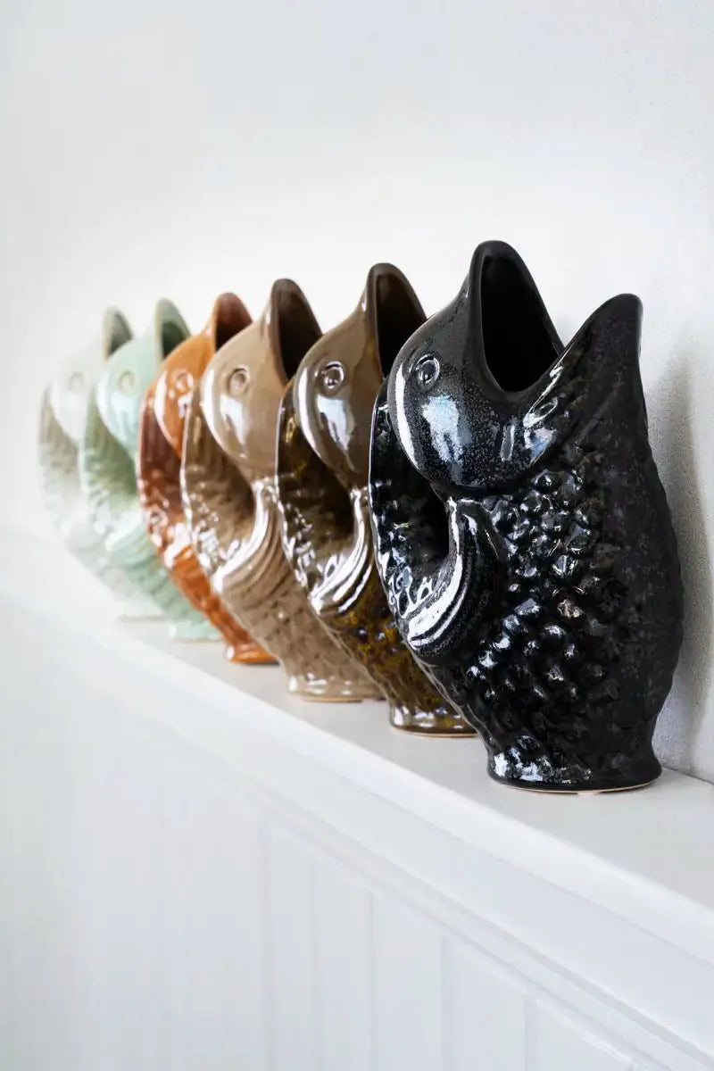 Row of ceramic fish-shaped vases in various colours on a white surface.