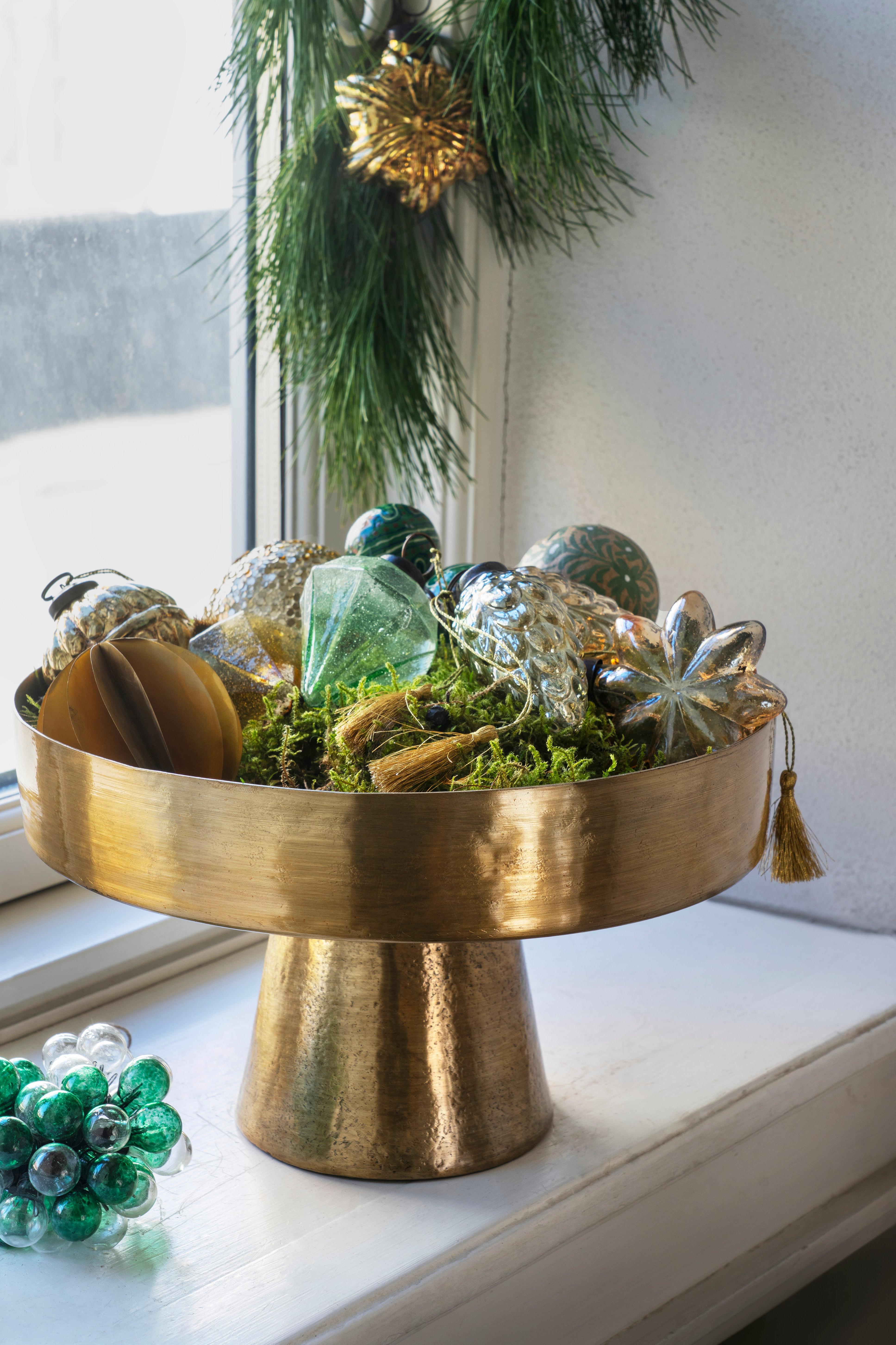 Decorative brass bowl with Christmas ornaments on a windowsill