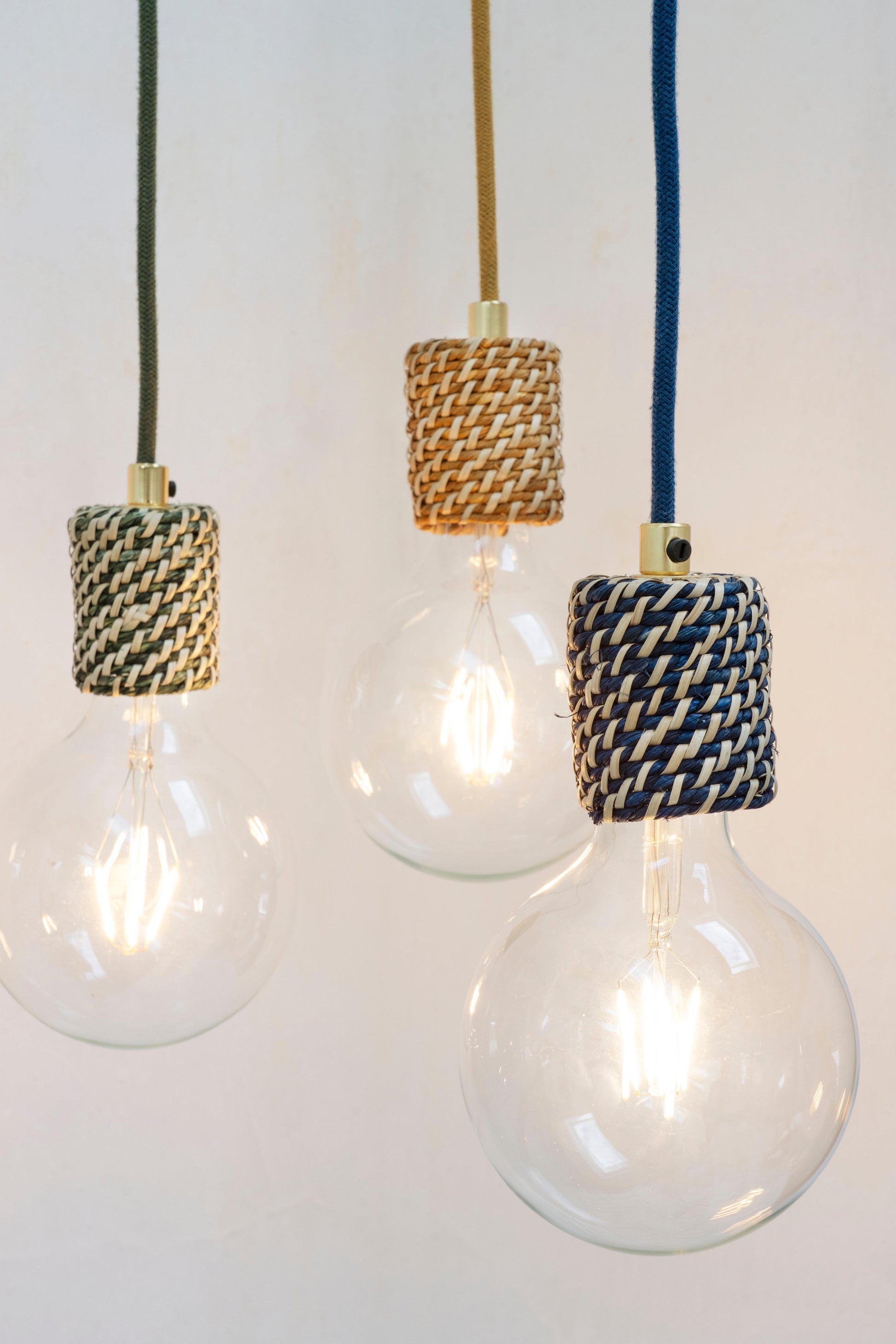 Three light bulbs with woven Madam Stoltz covers hanging against a white background