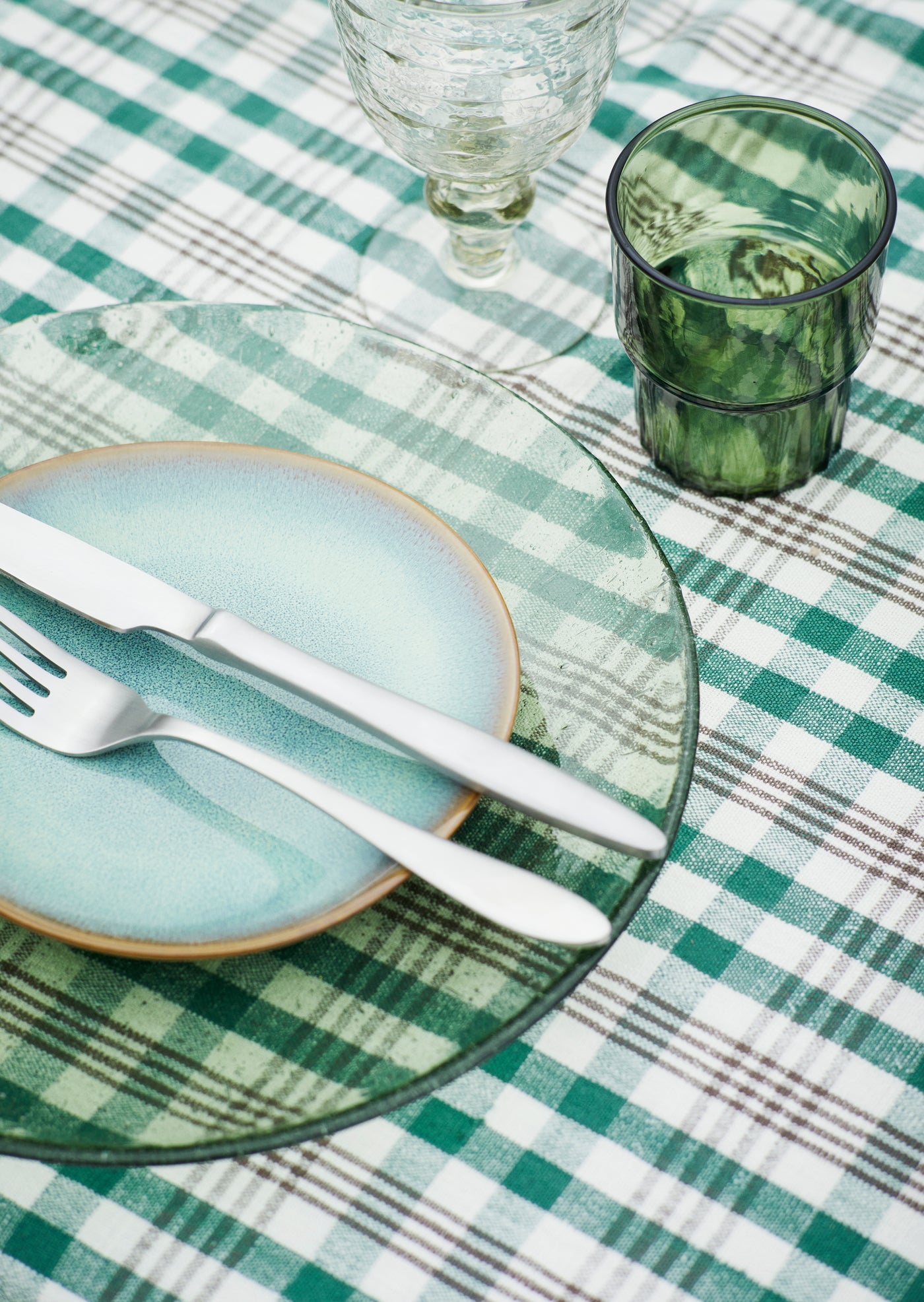 Table setting with green and white checkered tablecloth, ceramic plates, and glasses.