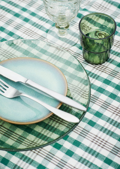 Table setting with green and white checkered tablecloth, ceramic plates, and glasses.