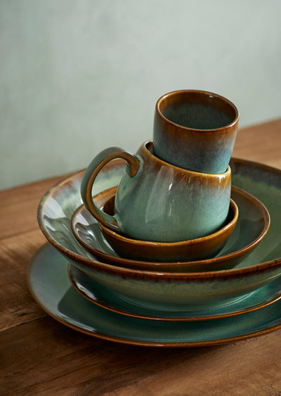 Stack of ceramic cups and saucers on a wooden surface with a neutral background
