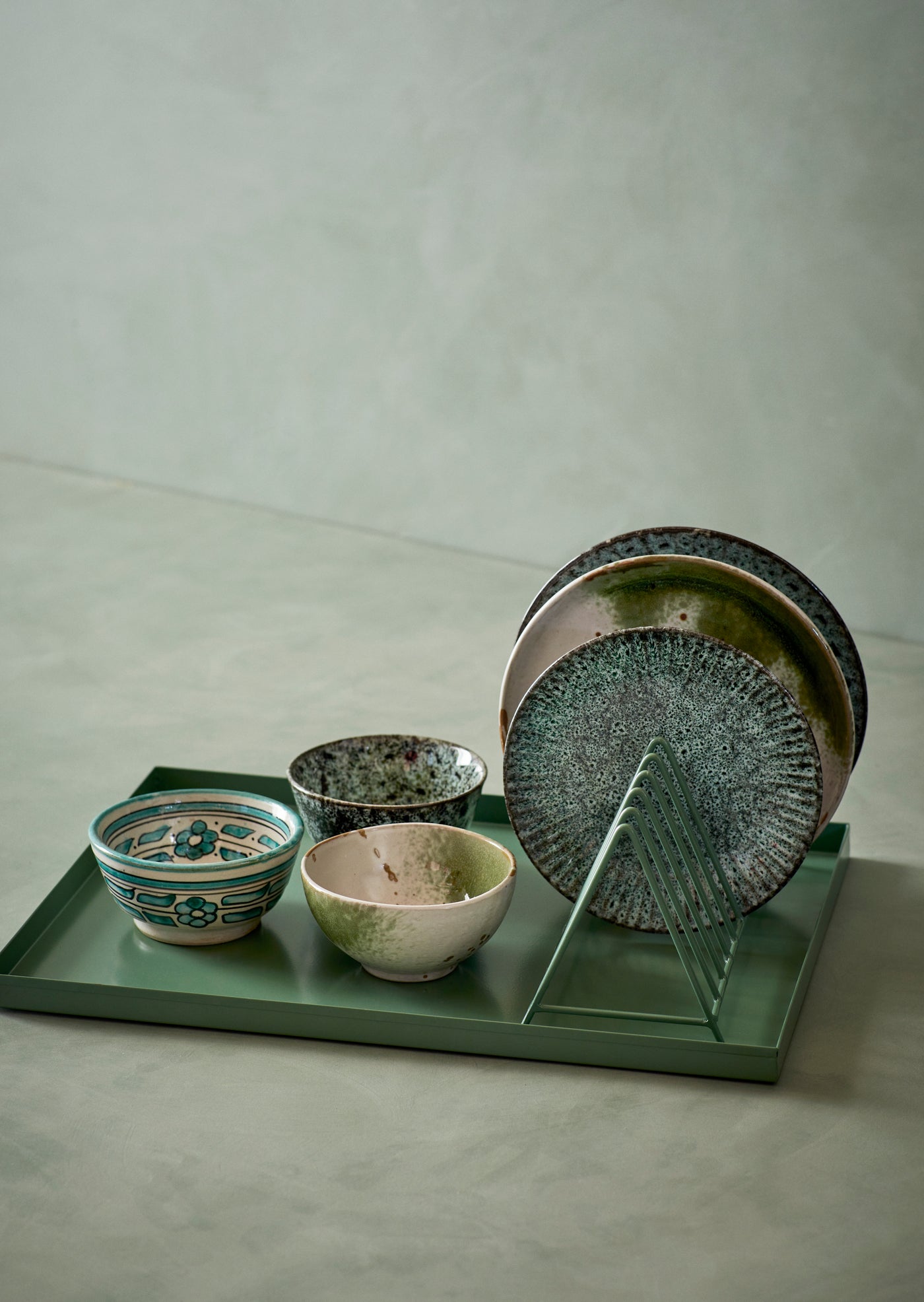 Set of ceramic bowls and plates on a green tray against a neutral background