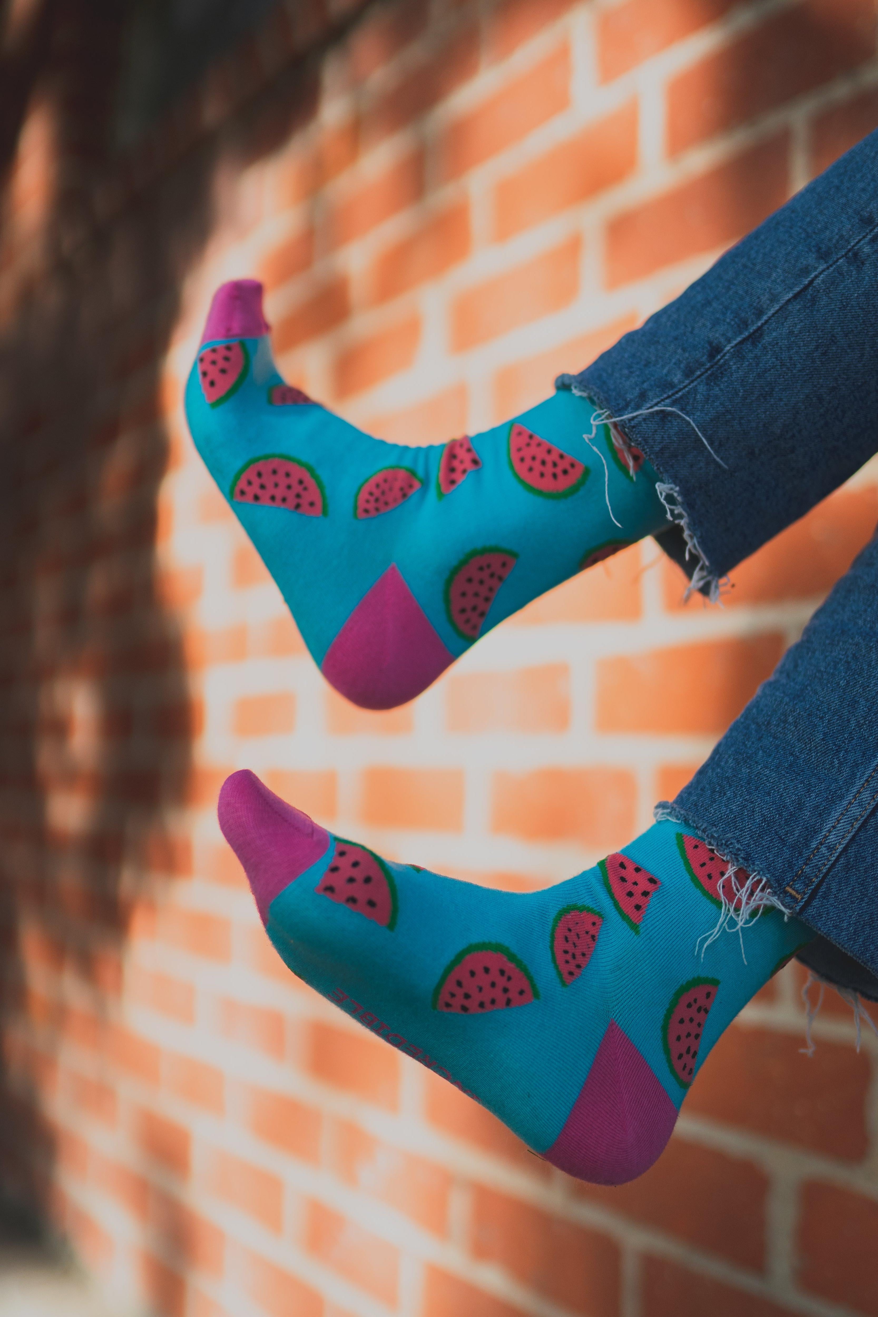 Teal socks with watermelon design worn by a person against a brick wall.