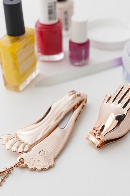 Copper foot and hand-shaped clips on a light surface with nail polish bottles in the background.