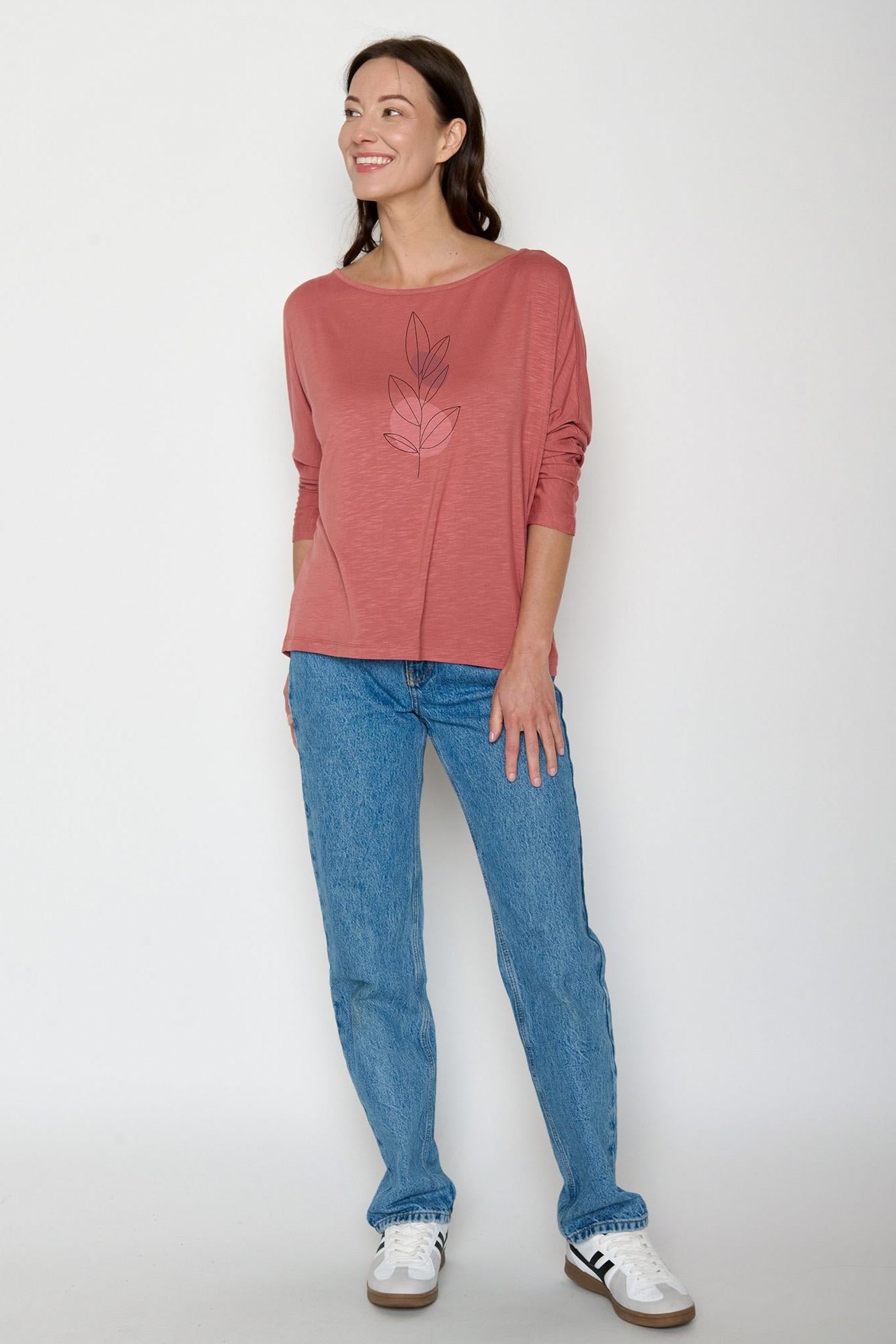 Woman wearing a pink eco-vero top and blue jeans on a white background