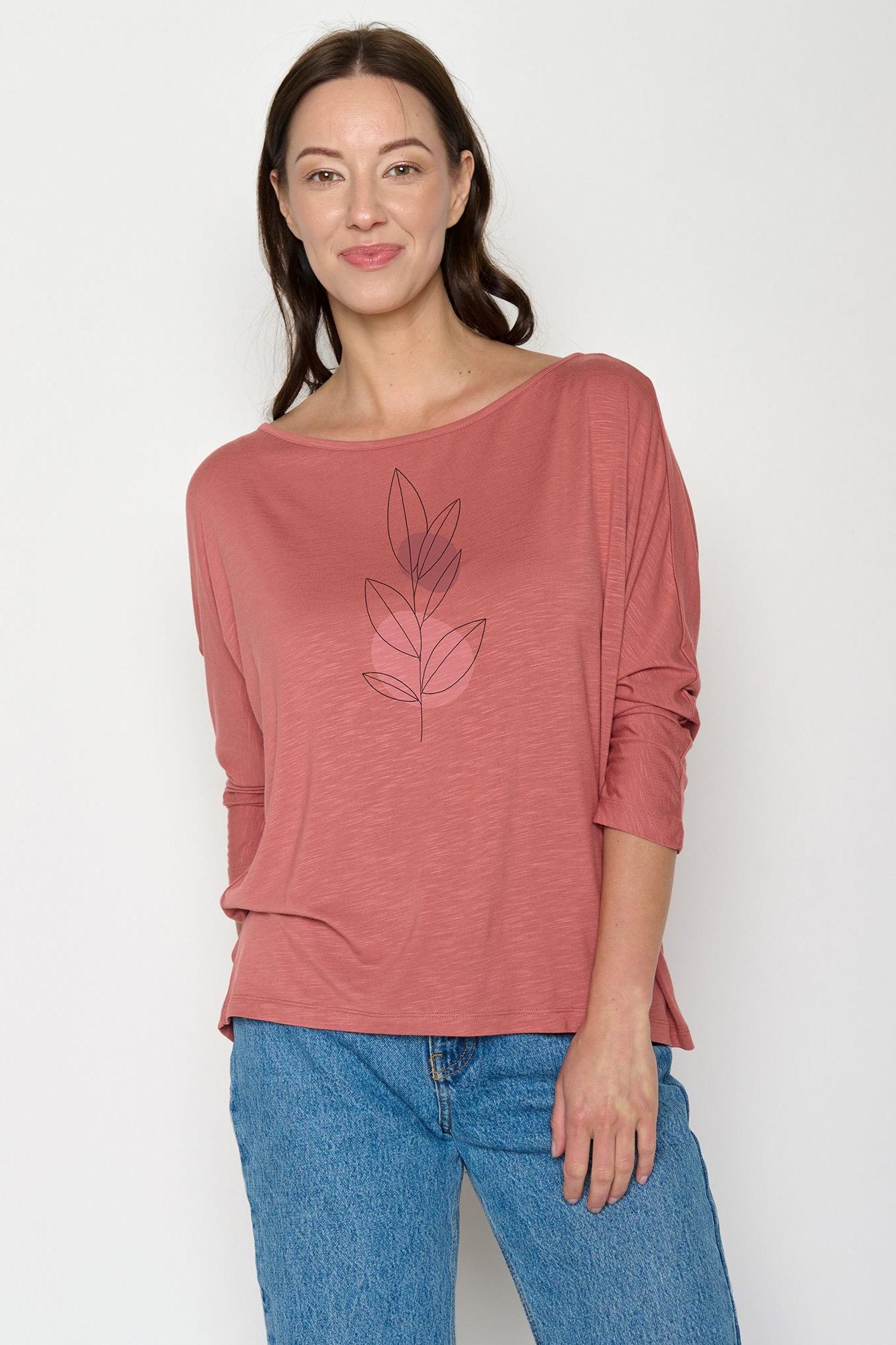 Woman wearing a pink long-sleeve top with a leaf design and blue jeans on a white background