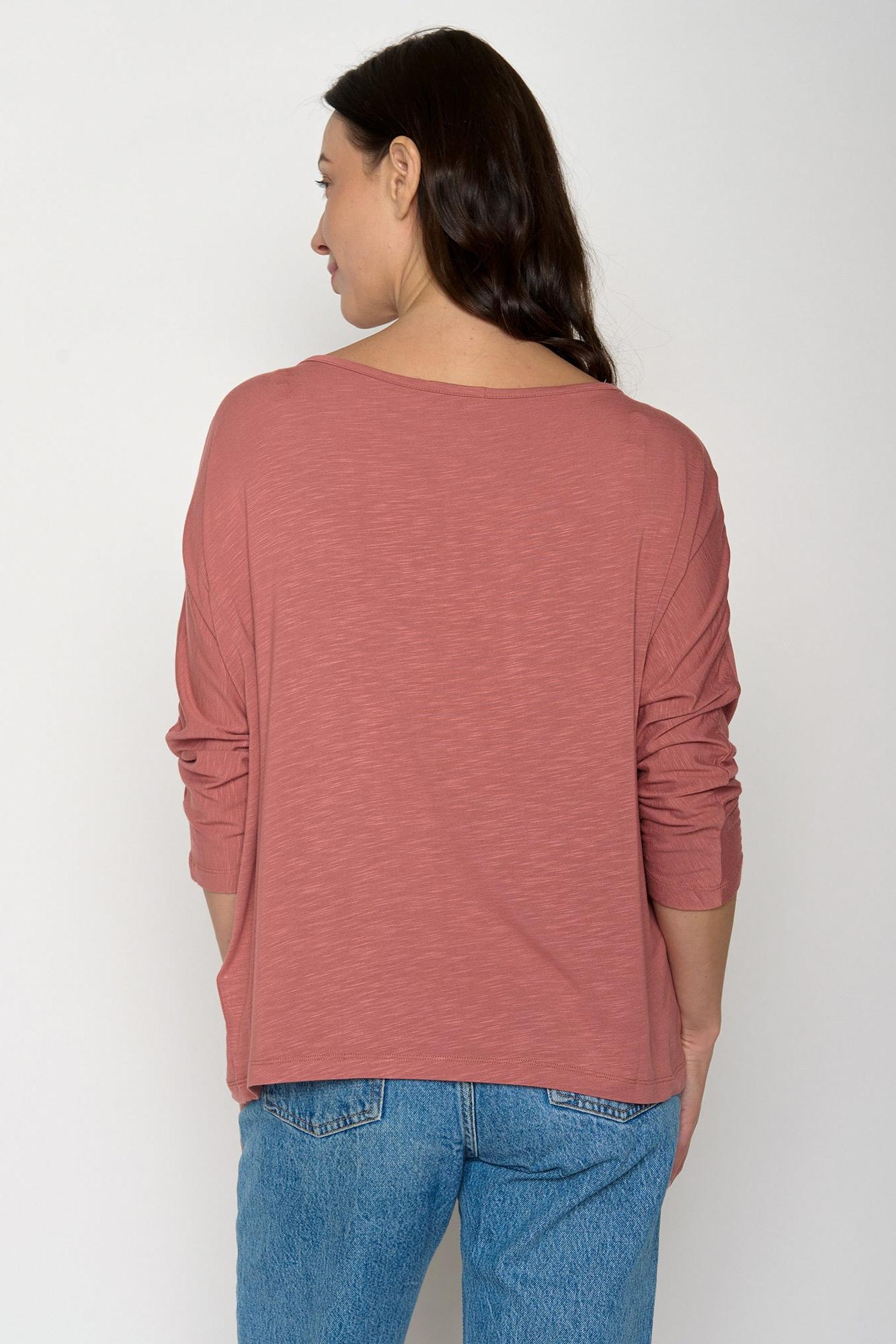 Woman wearing a long-sleeve rust-colored top and blue jeans against a white background