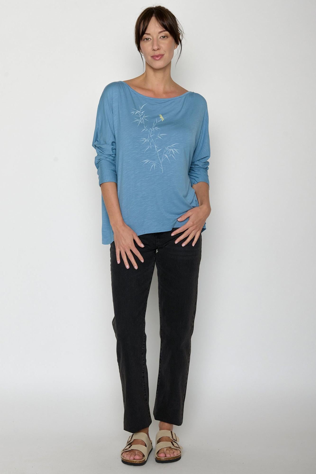 Woman wearing a Greenbomb blue top and black pants on a white background