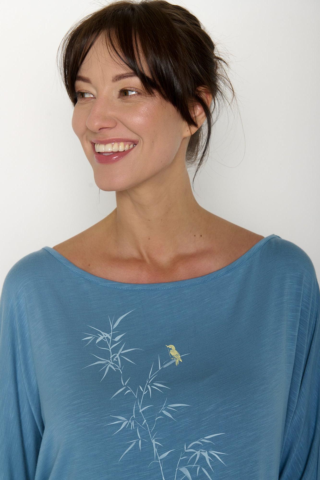 Woman wearing a blue longsleeved shirt with a bamboo design against a white background