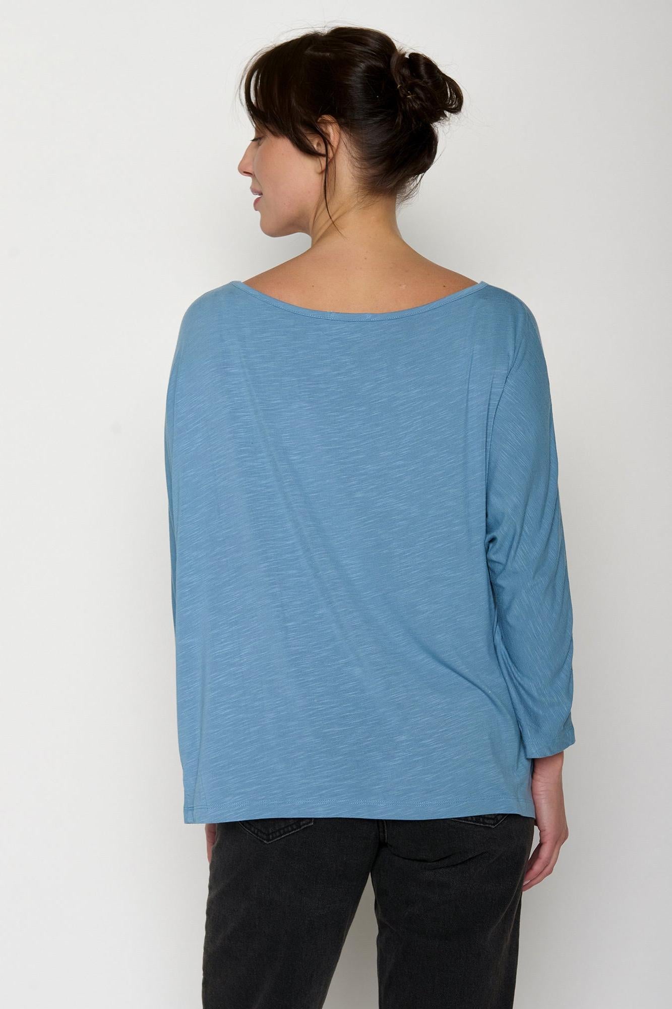 Woman wearing a blue long-sleeve top against a white background