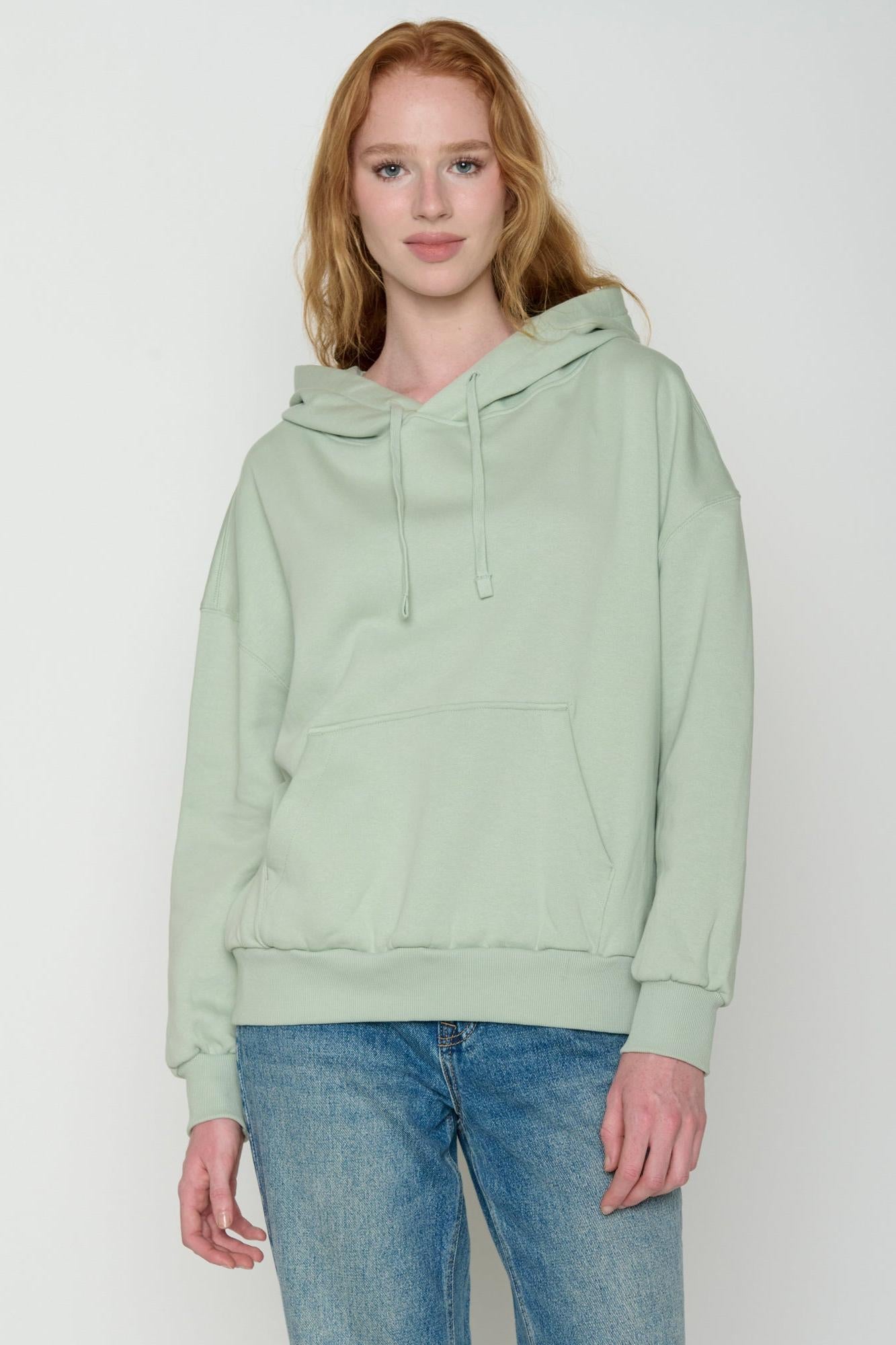 Model wearing a light green organic cotton hoodie and blue jeans on a white background